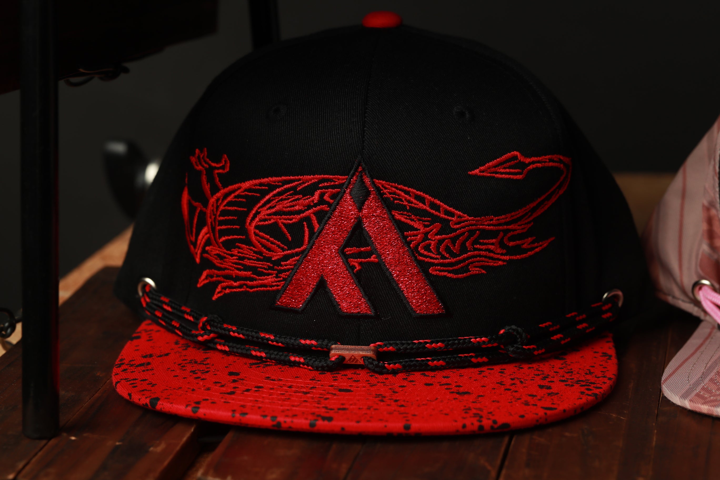 A black baseball cap with a red dragon design on it, sitting on a wooden surface.