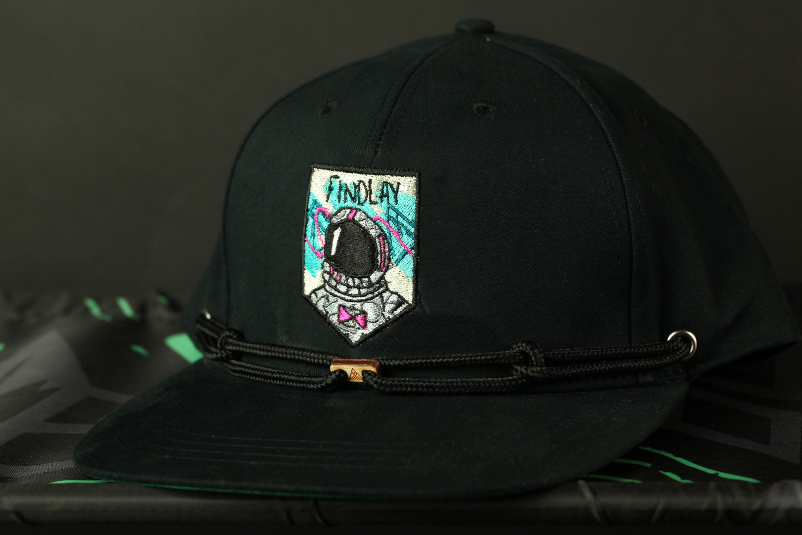 A black baseball cap with a colorful patch featuring an astronaut's helmet and the word "FINOLAY" on it.