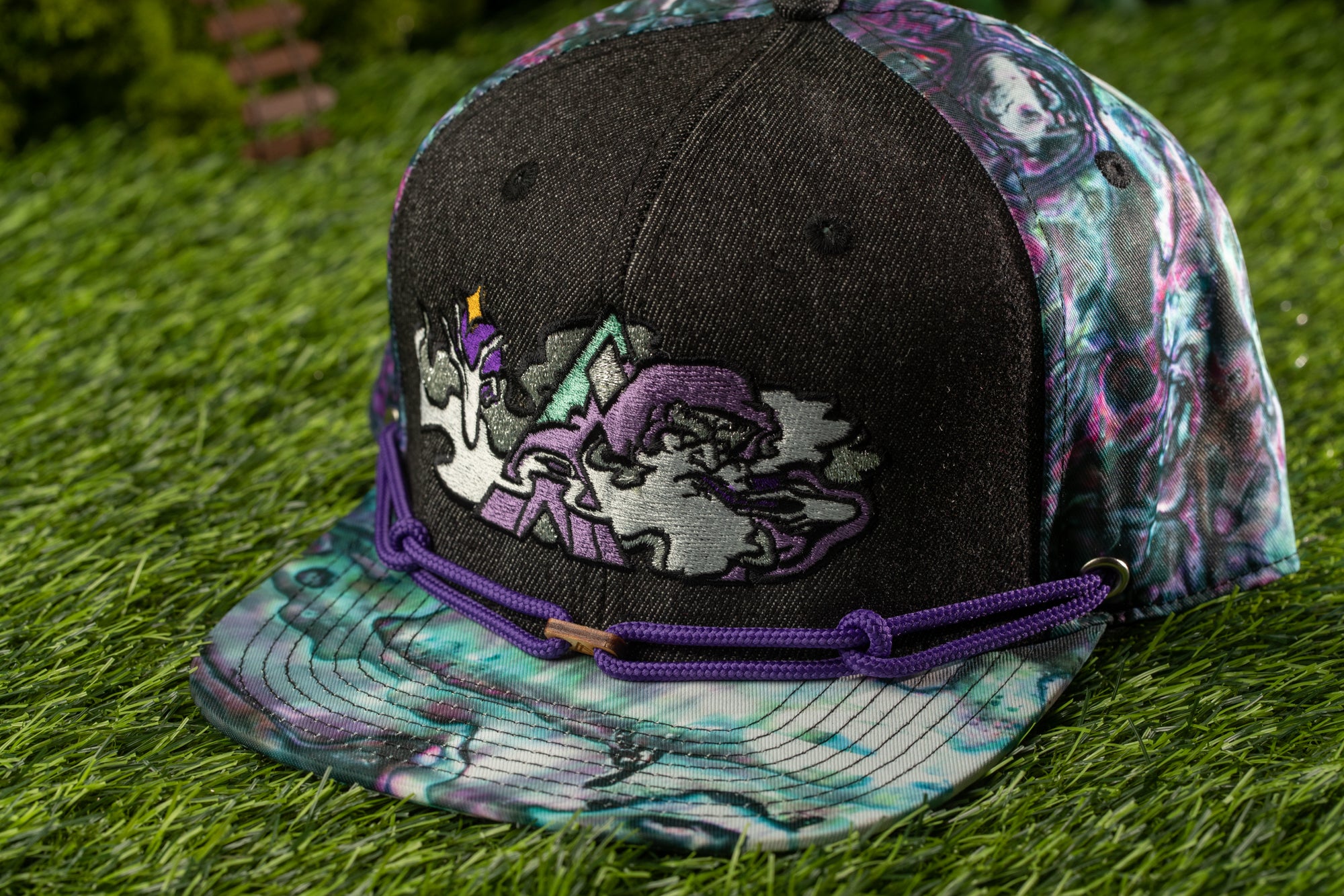 A colorful, patterned baseball cap with a unicorn design on the front, resting on a grassy surface.
