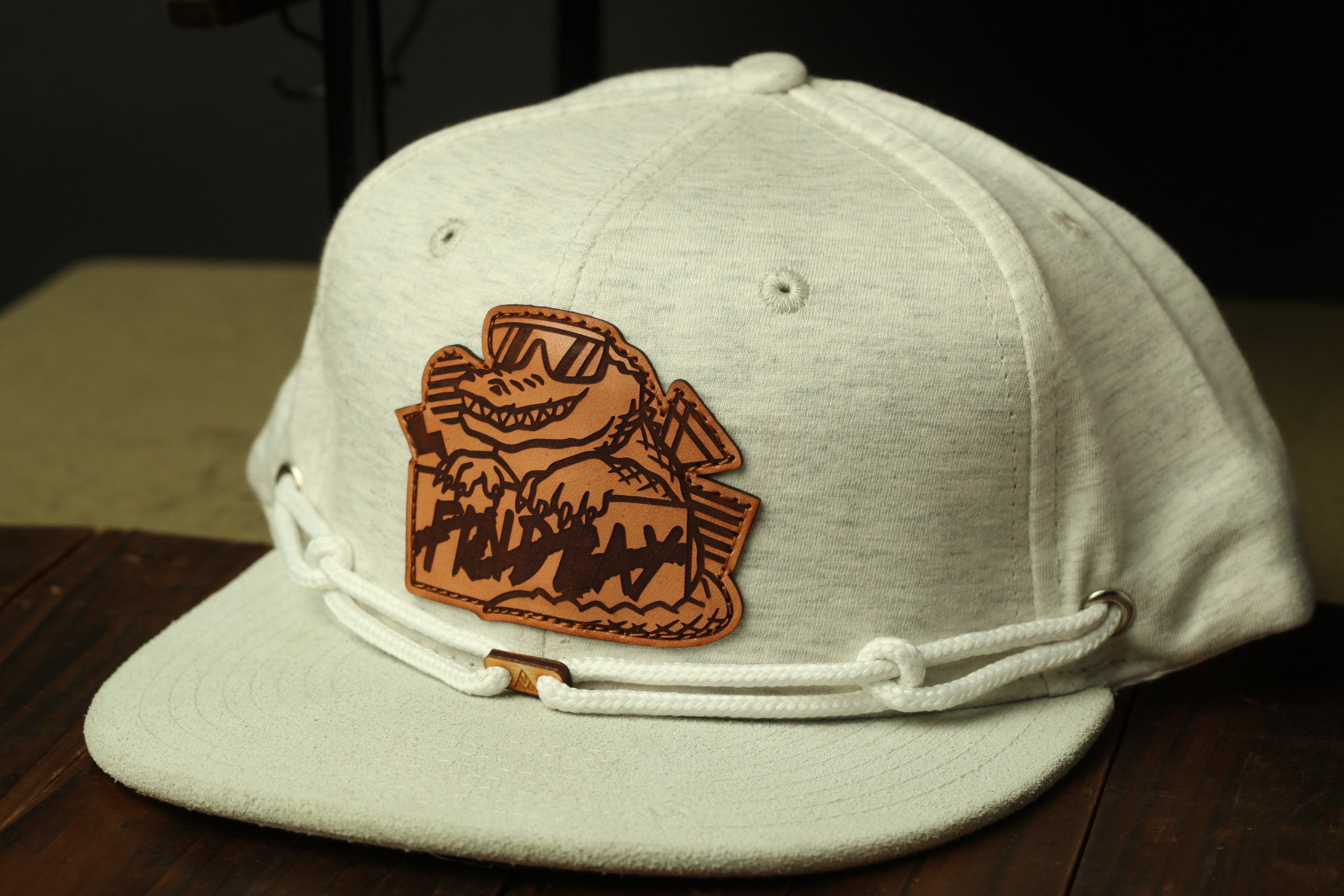 A white baseball cap with a brown leather patch featuring a cartoon character on it, placed on a wooden surface.