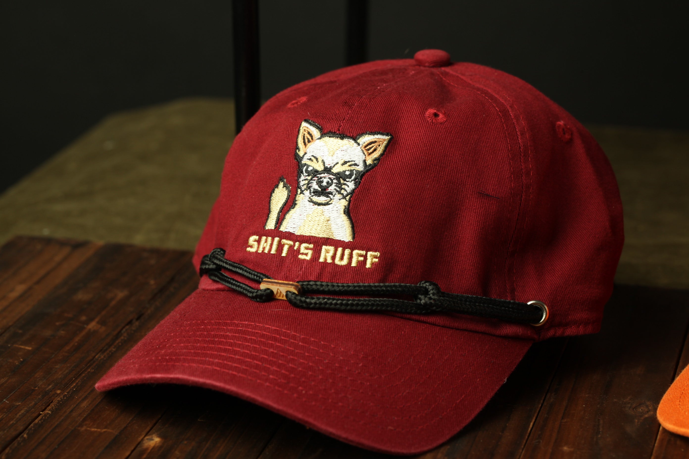 A red baseball cap with a cartoon dog and the text "SHIT'S RUFF" printed on it.