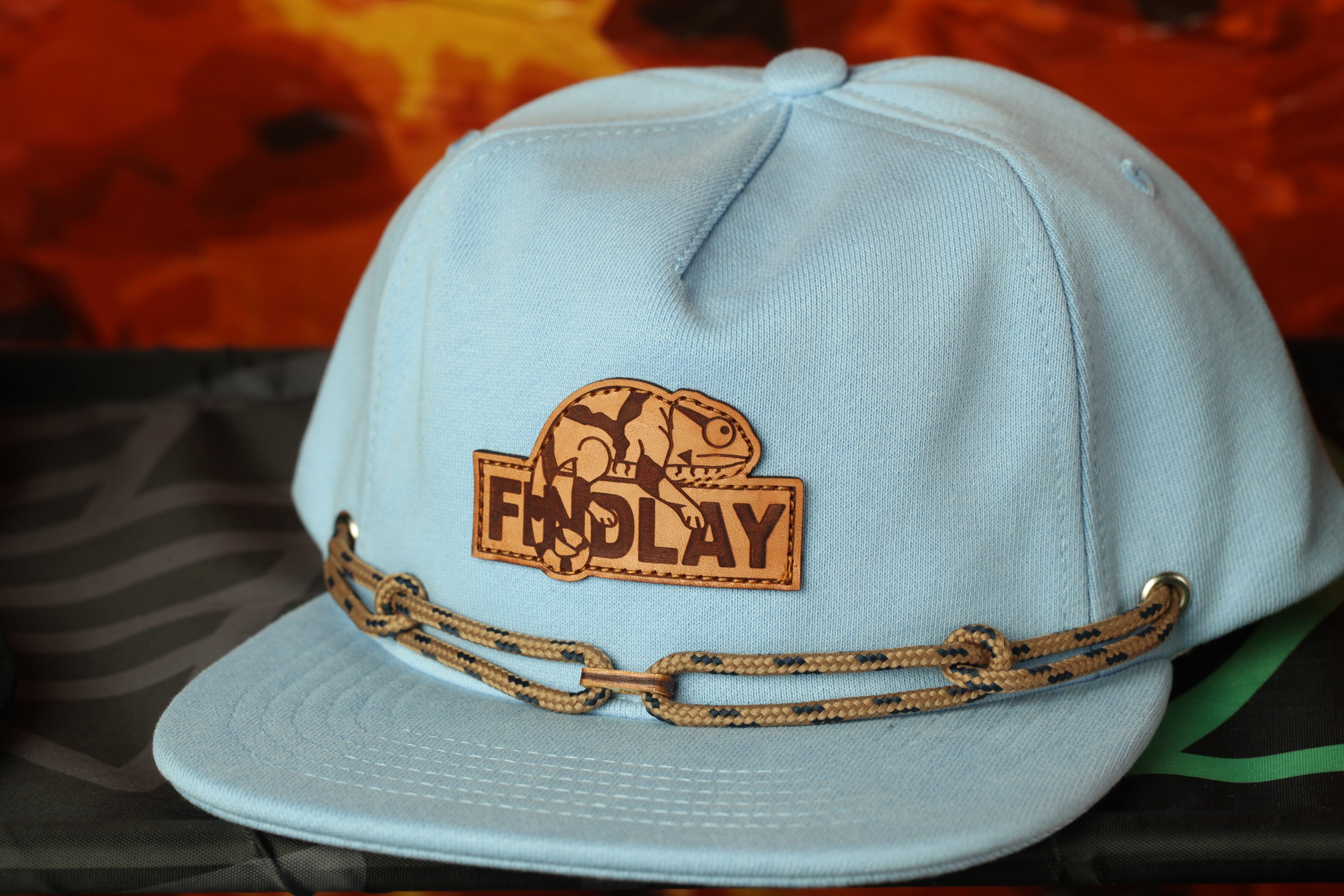A light blue baseball cap with a brown leather patch that says "FIND LAY" and a chain strap.