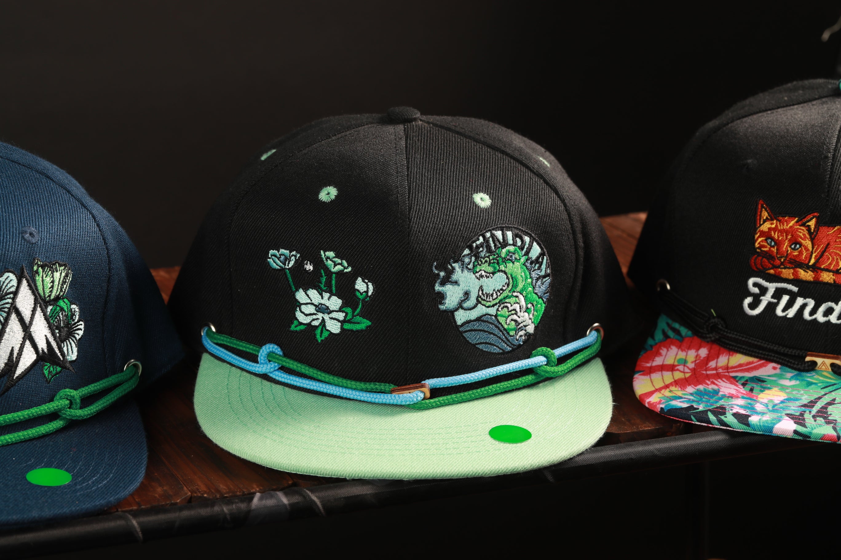 Three colorful baseball caps with various designs and patterns, including floral and animal motifs, are displayed on a shelf.