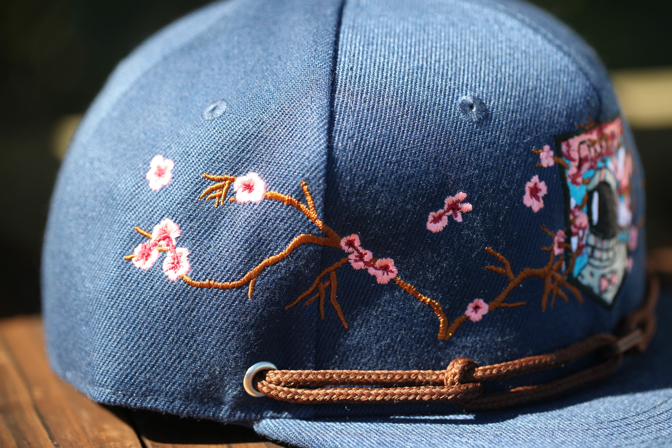 A close-up view of a blue baseball cap with a floral embroidered design on the front.