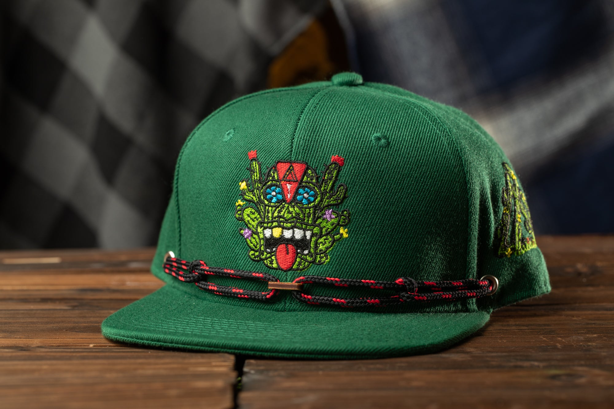 A green baseball cap with a colorful, cartoonish design on the front, featuring a face with a red and green color scheme.