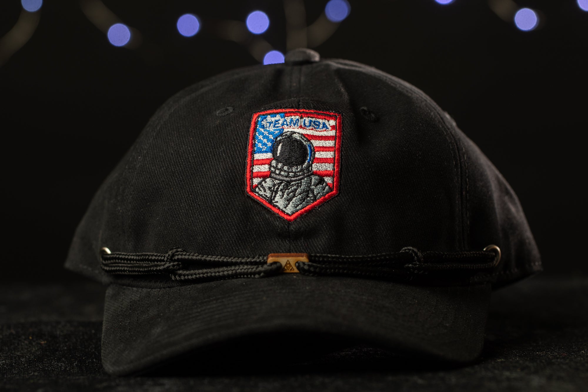 A black baseball cap with a red and blue patch on the front, featuring an image of a person in a spacesuit and the text "TEAM USA" on the patch.
