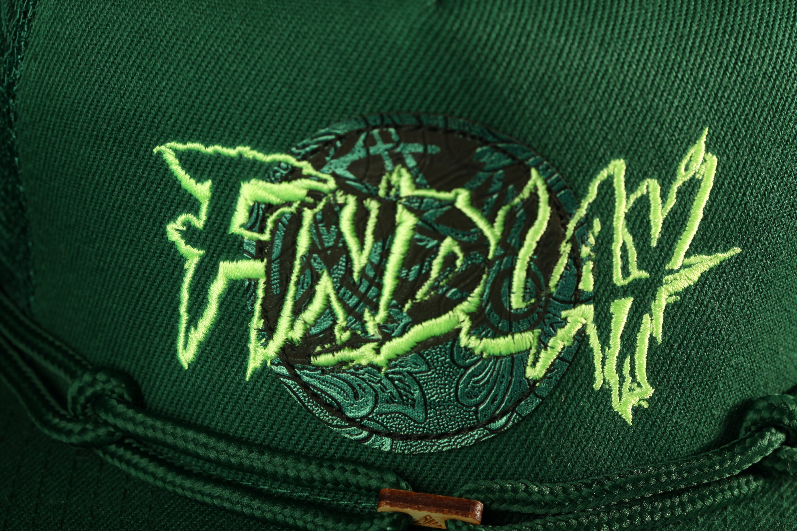 a close-up view of a dark green fabric with a unique embroidered design on it. The design includes a circular motif with a green and black pattern, and the word "FIND" is prominently displayed in a stylized font.