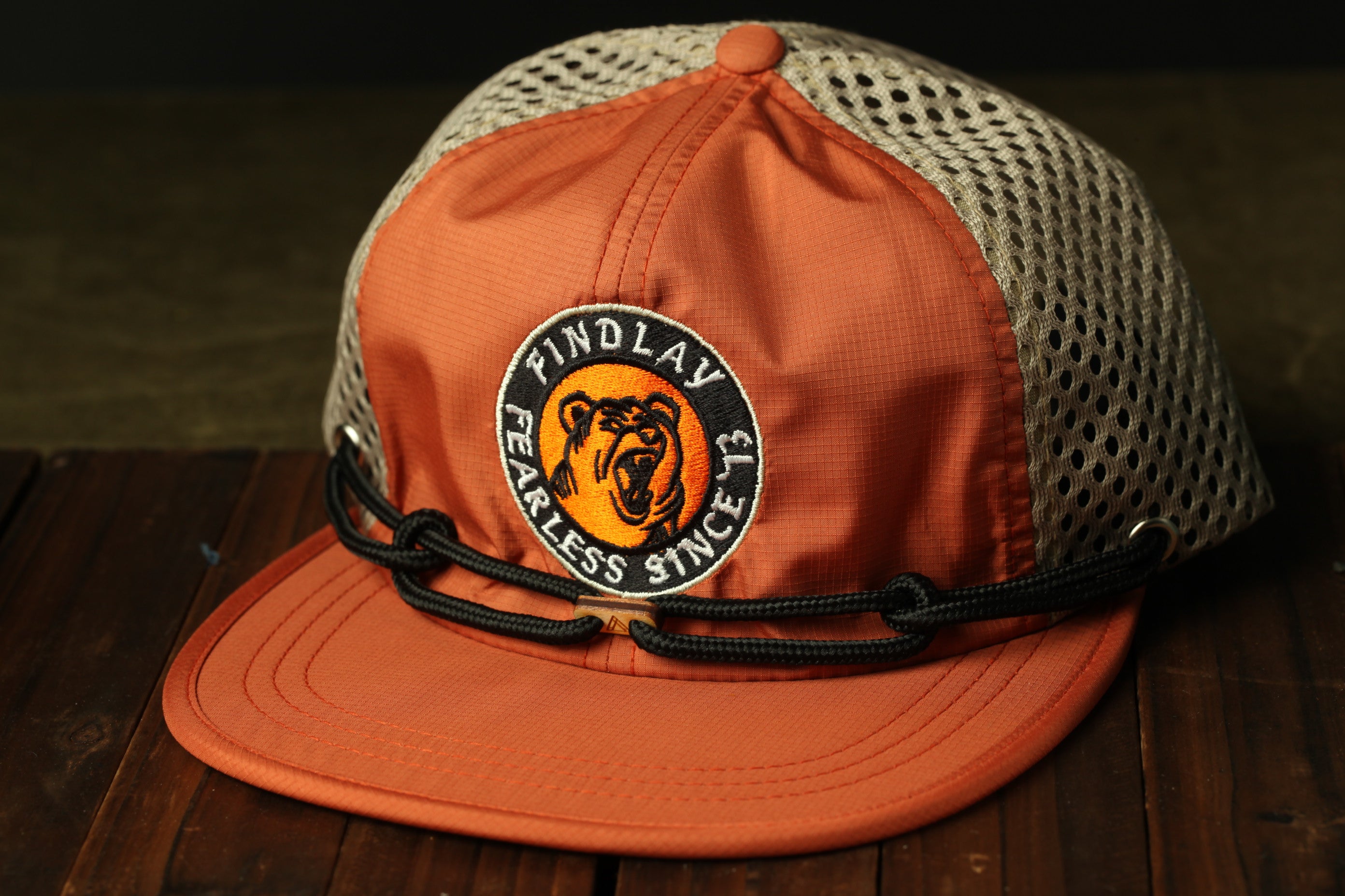 An orange baseball cap with a mesh panel and a black strap, featuring a logo with a bear's face and the text "FINDLAW FEARLESS SINCE 1973" on it.