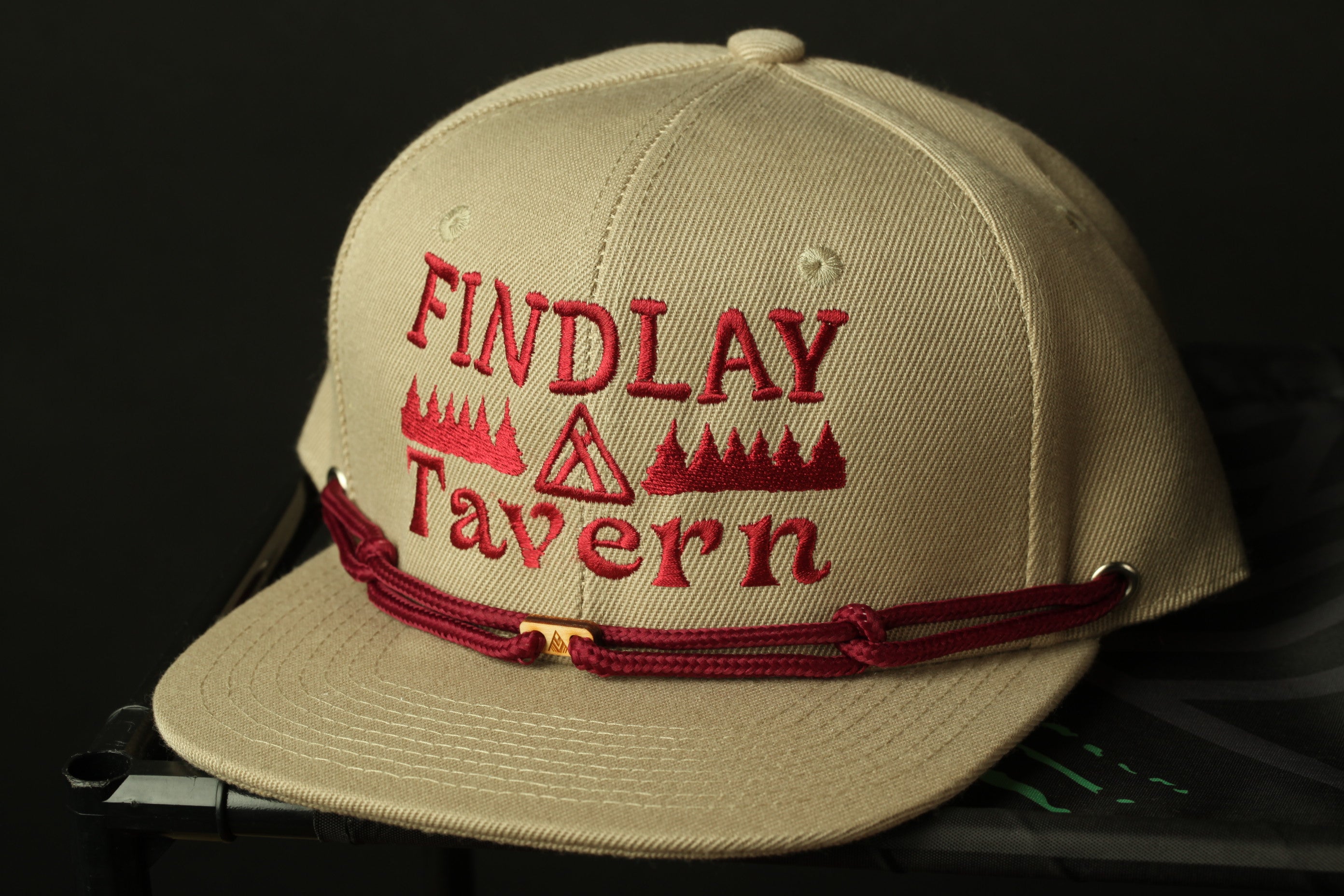 A beige baseball cap with red embroidered text and a red string around the brim.