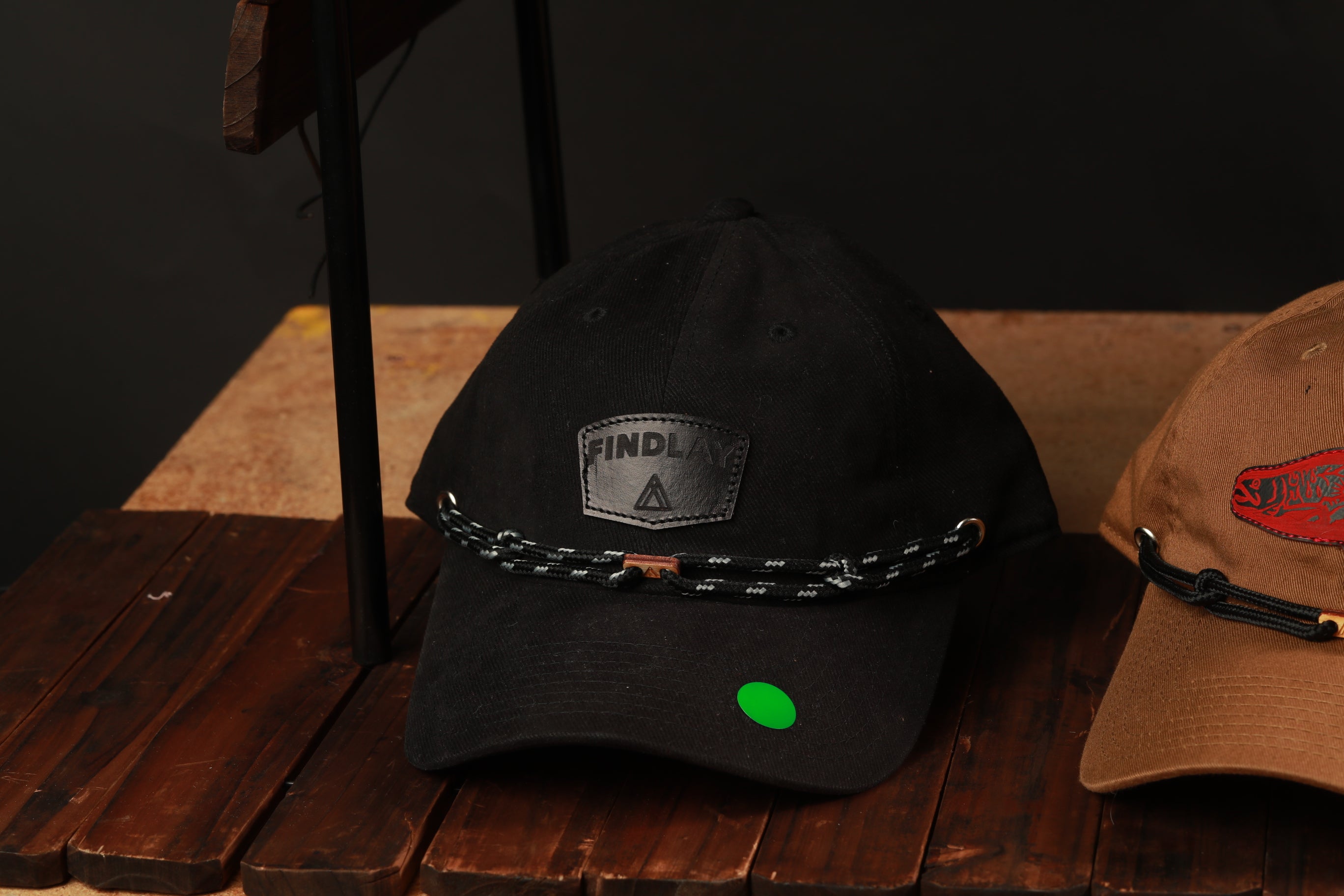 Two baseball caps are displayed on a wooden surface, one black and one brown.