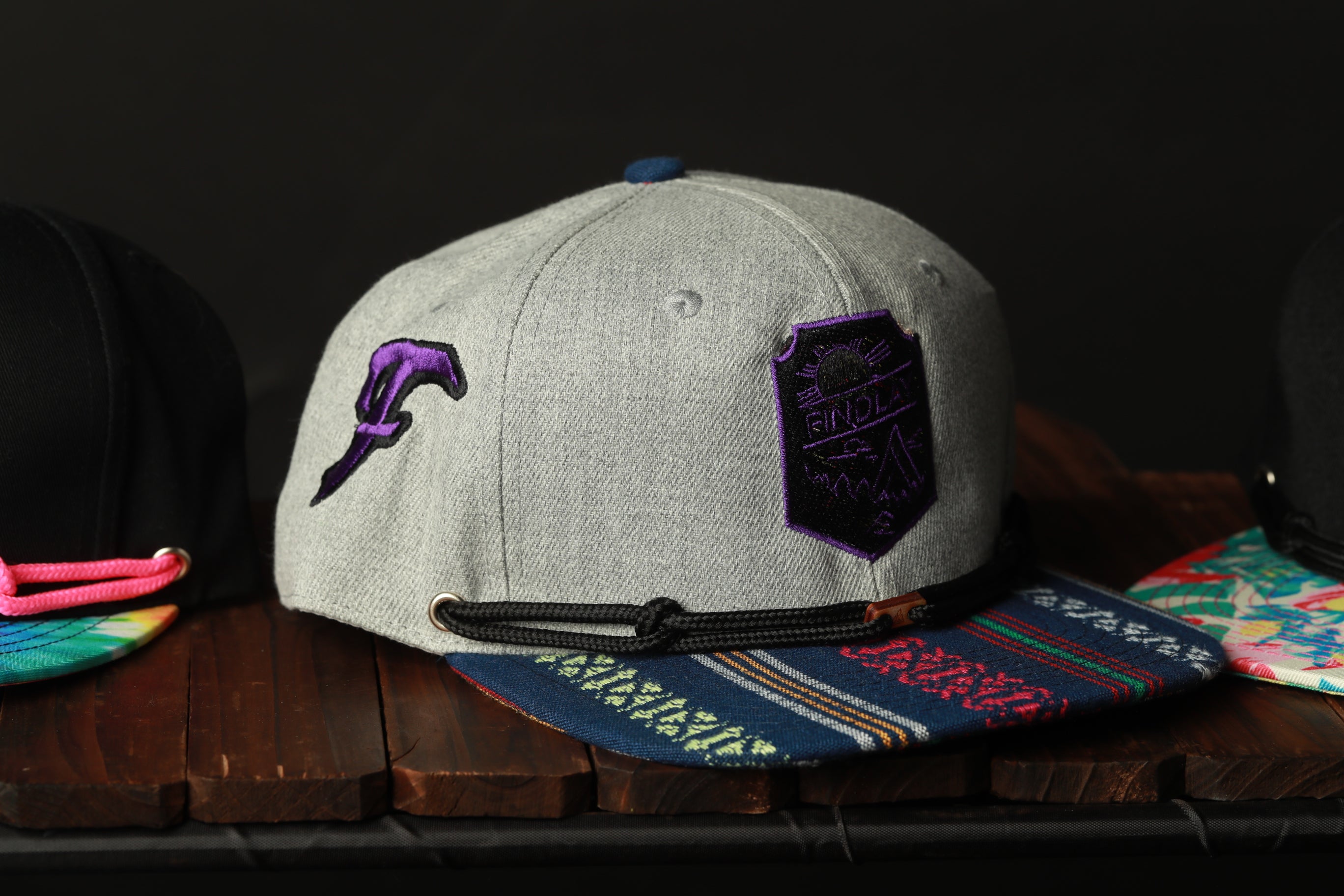 A gray baseball cap with a purple and black patch on the front, sitting on a wooden surface.