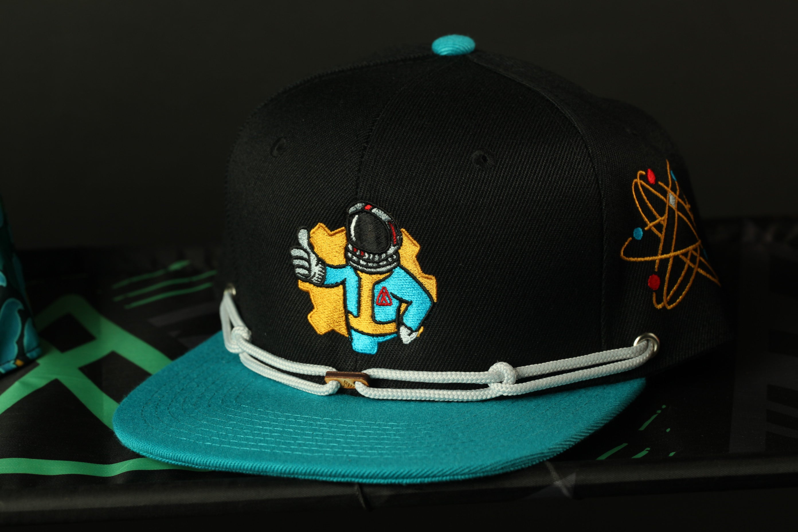 A black baseball cap with a colorful embroidered design of an astronaut on the front.