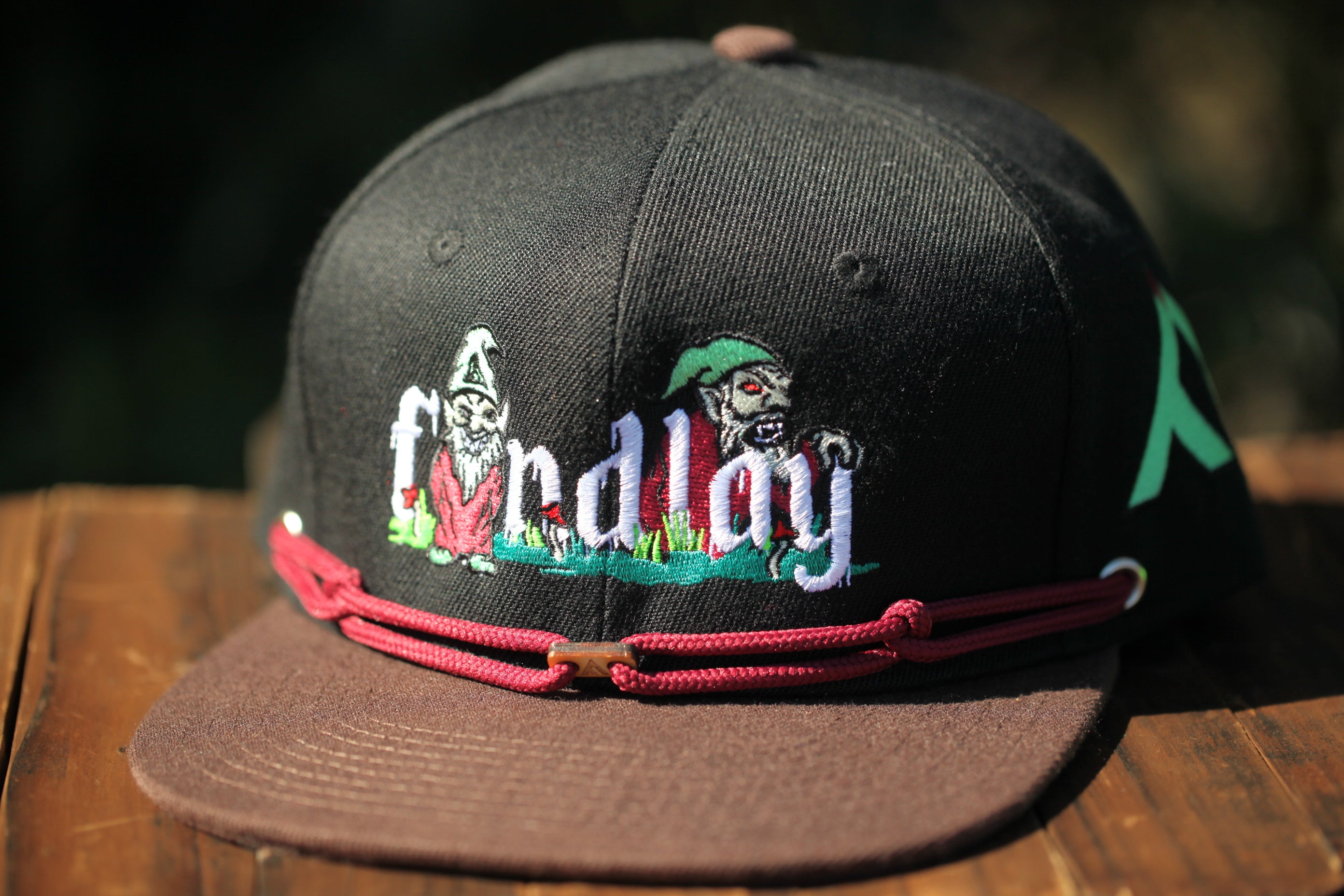 A black baseball cap with a red string and a graphic design on it, sitting on a wooden surface.