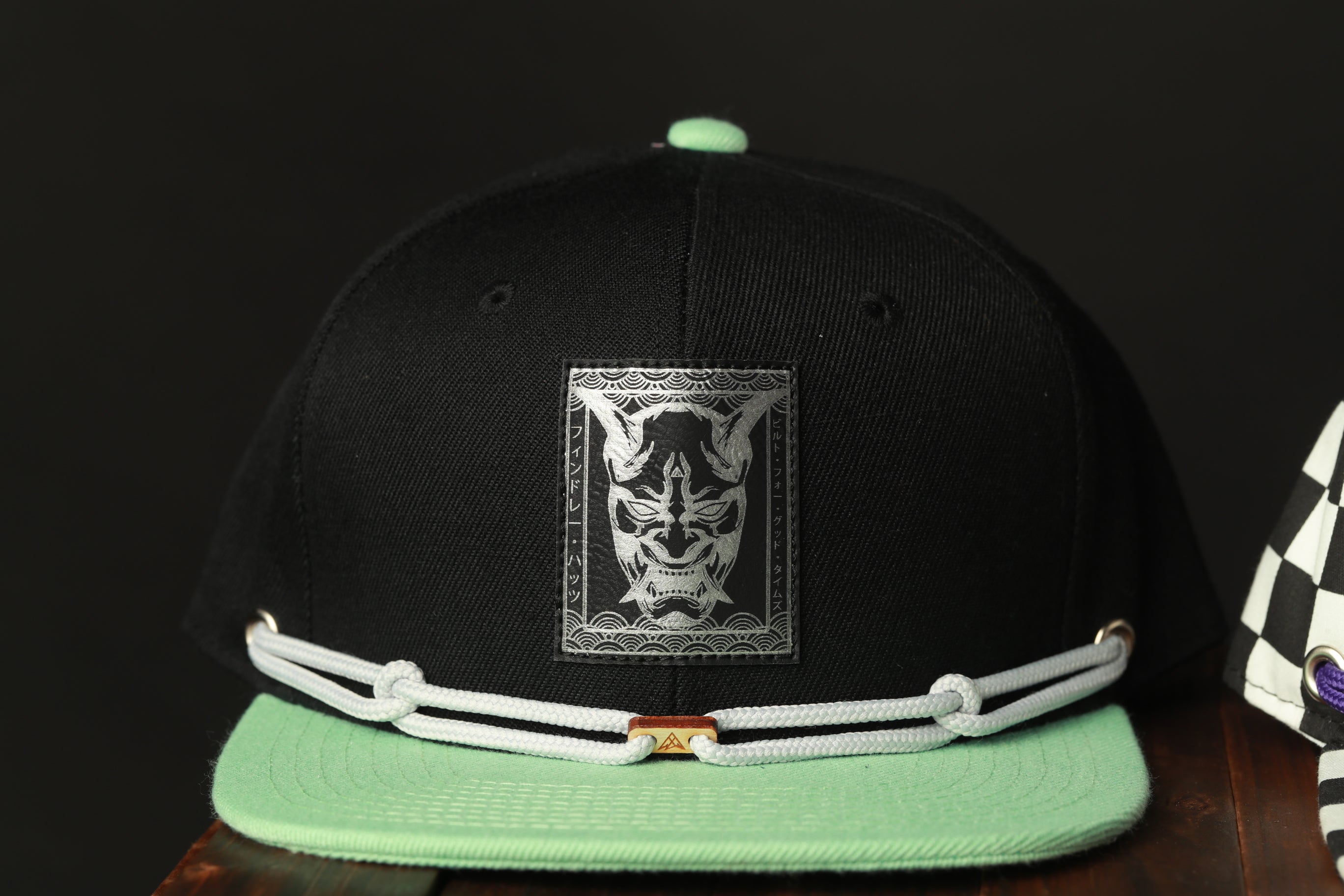 A black baseball cap with a white graphic design on the front, featuring a mask-like figure.