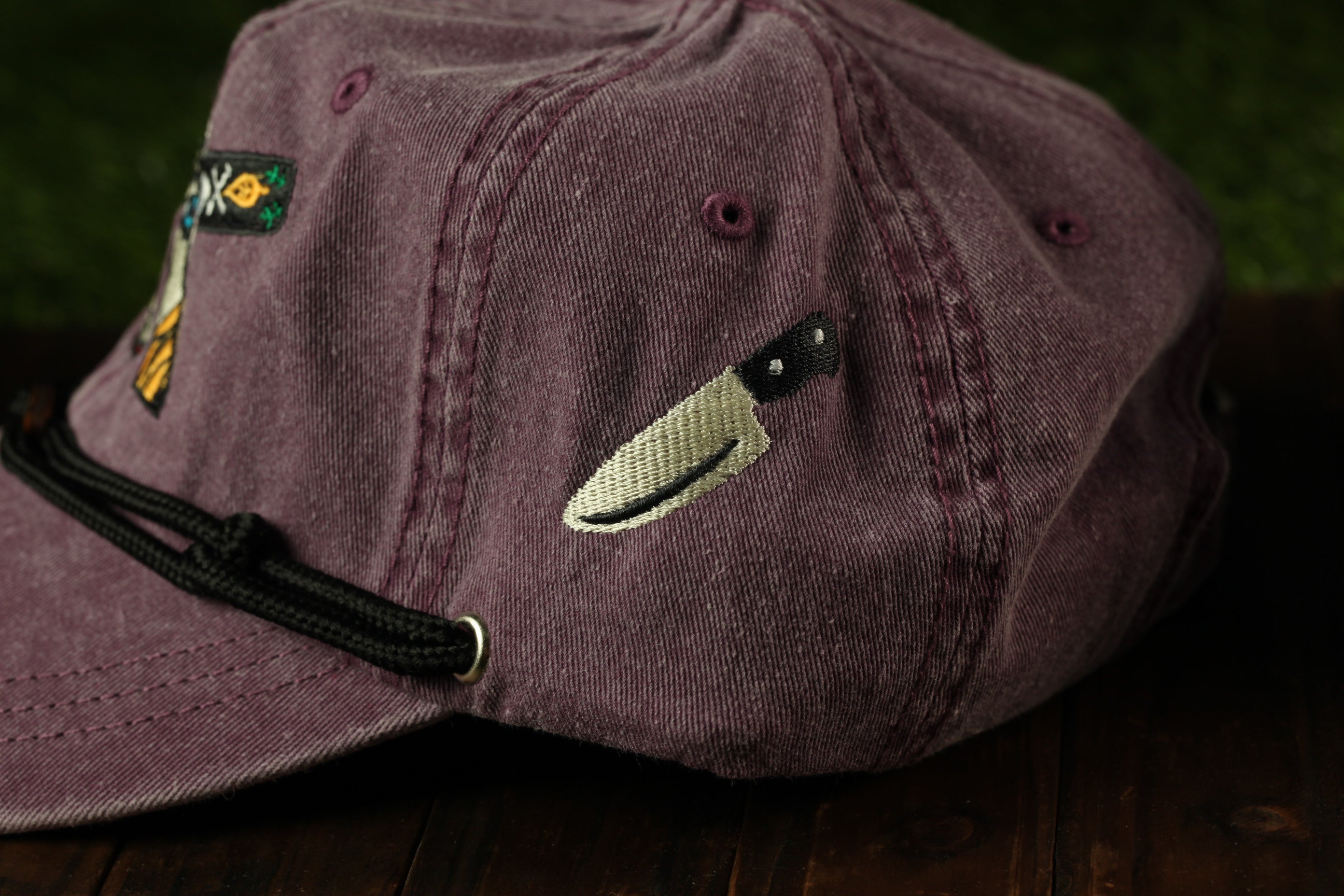 A close-up view of a purple baseball cap with a knife embroidered on it.