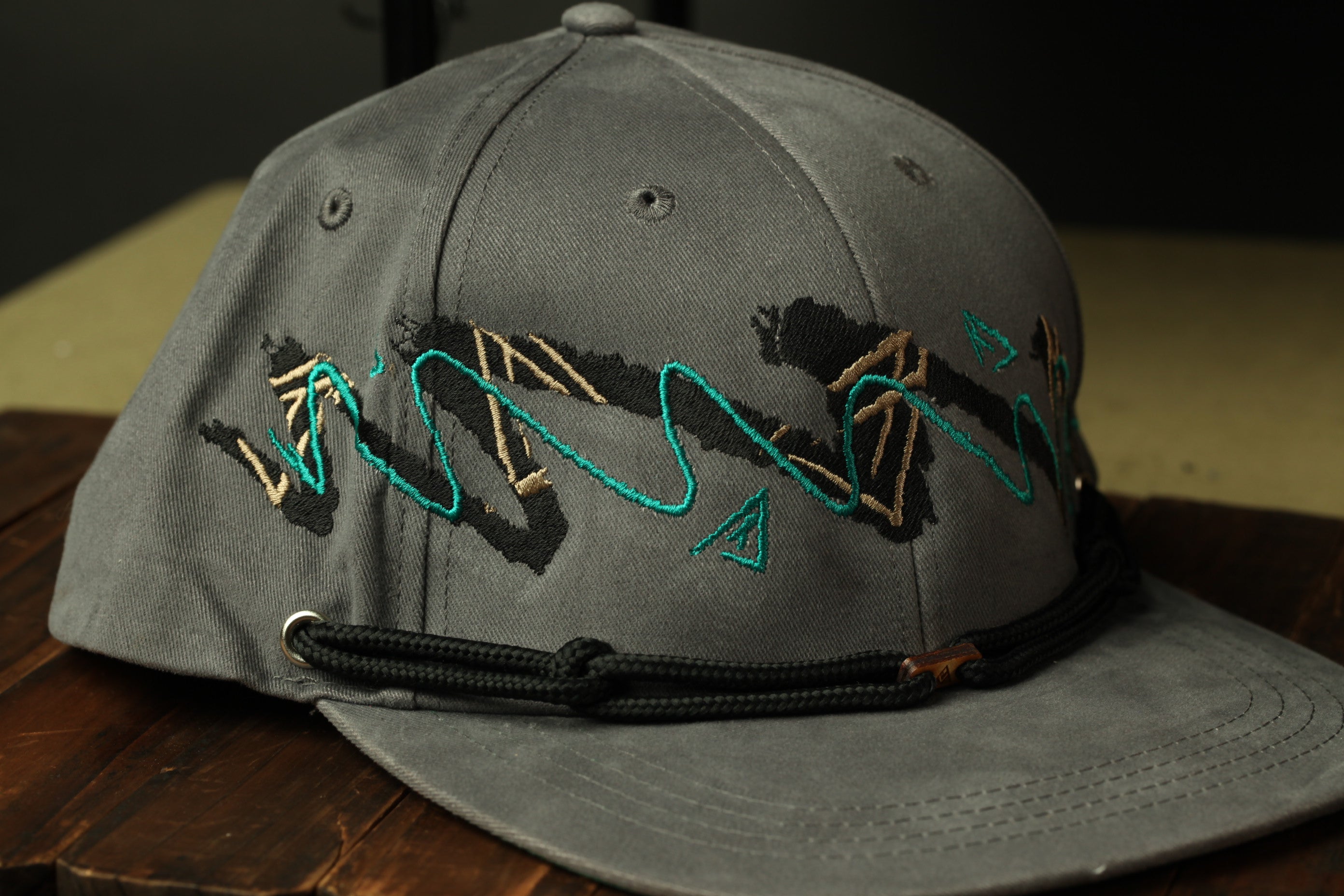 A gray baseball cap with a black strap and a unique embroidered design on the front.