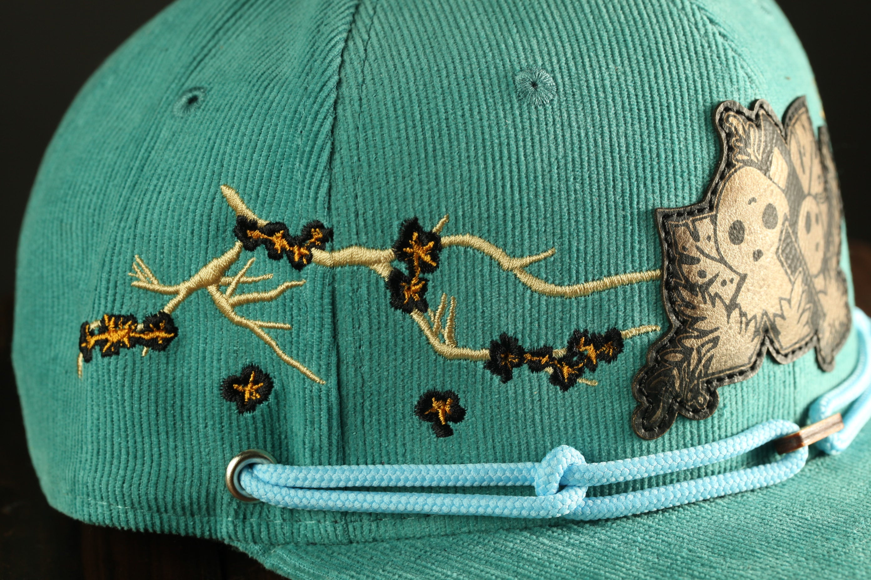 A close-up view of a turquoise baseball cap with a floral embroidered design on the front.