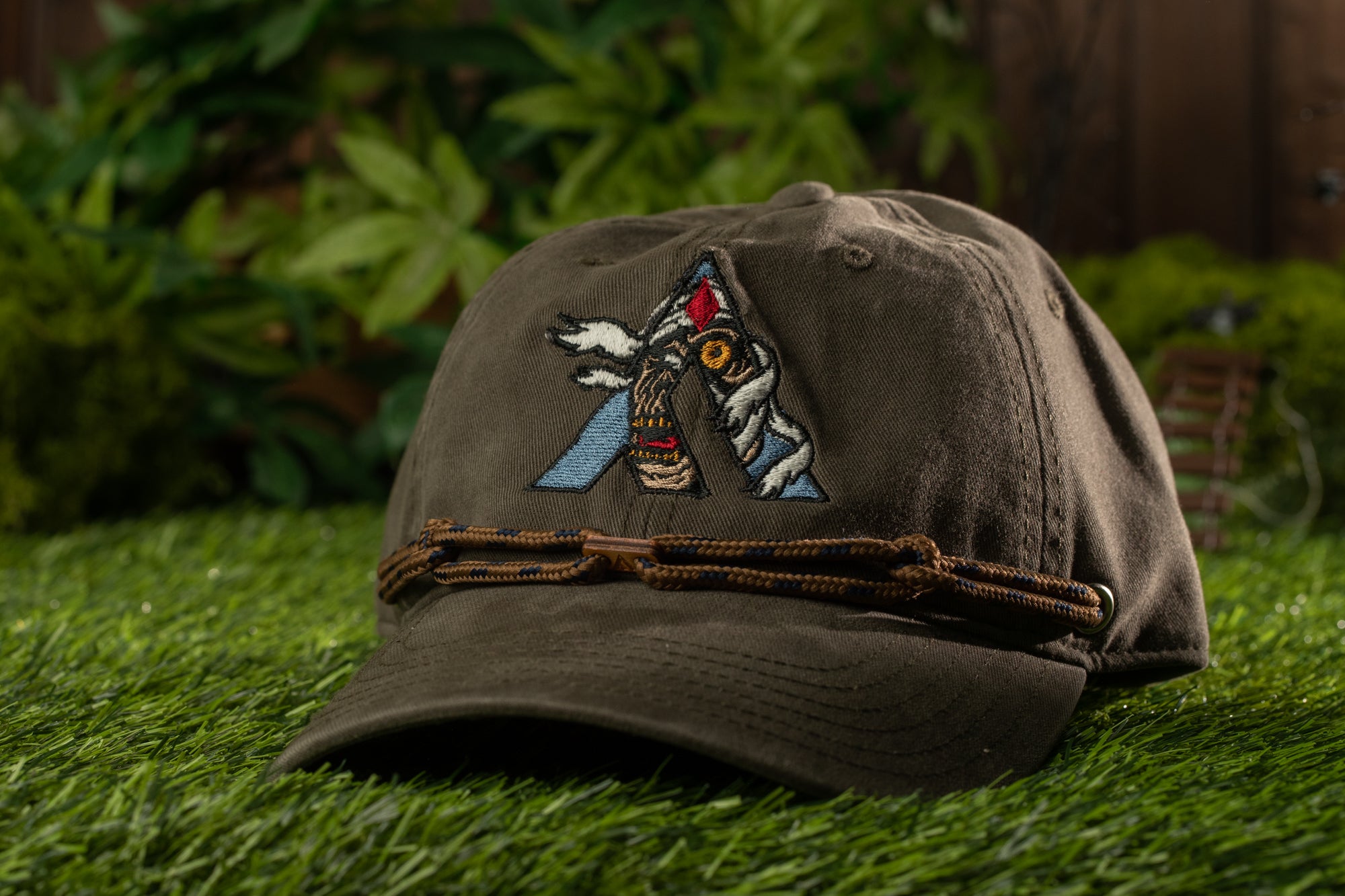 A brown baseball cap with a graphic design on it, placed on a grassy surface.