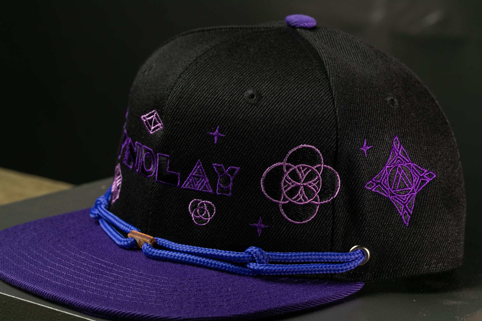 A black baseball cap with purple embroidered designs and text on it.