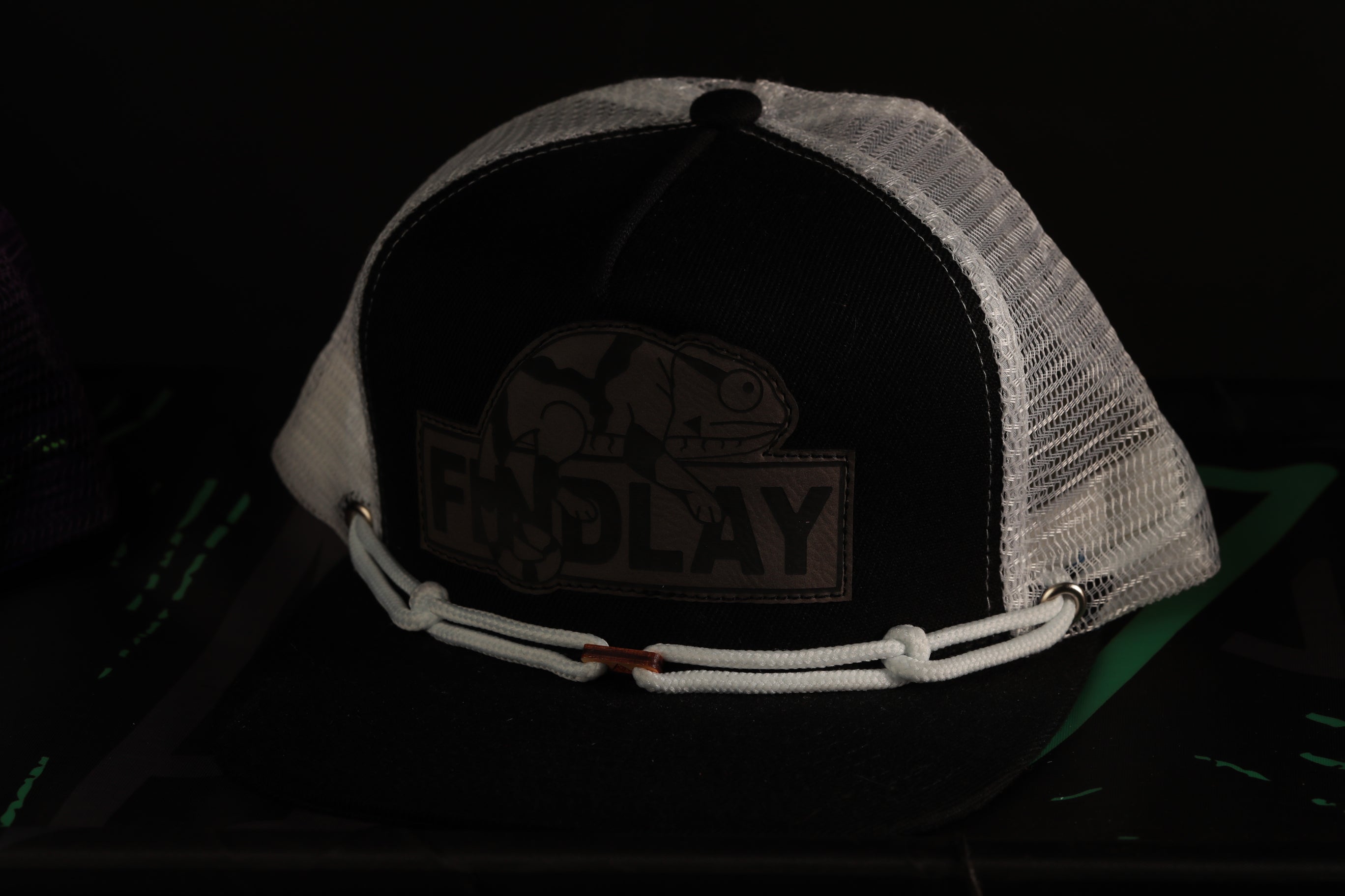 A black baseball cap with a mesh panel and a white strap, featuring a logo or emblem on the front.