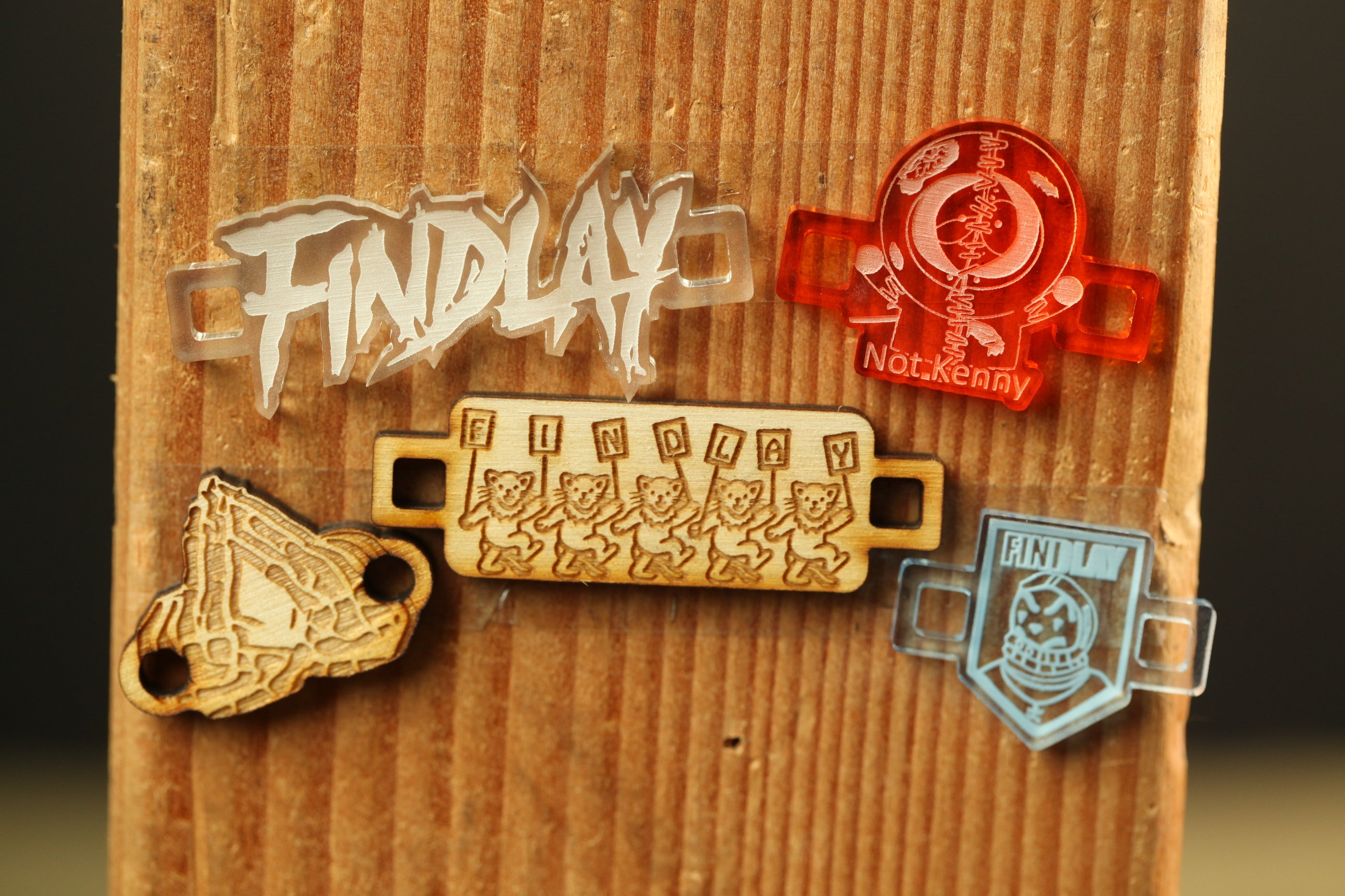 a wooden surface with various printed and engraved items, including a wooden tag with a bear design, a wooden tag with the word "Findlay" written on it, and a wooden tag with the word "Notekney" written on it.
