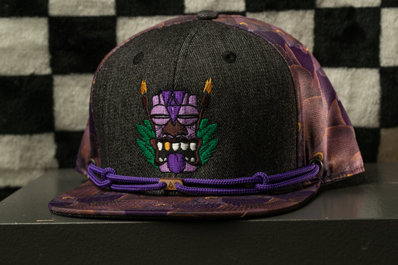 A black baseball cap with a purple and green design on the front, featuring a stylized face with horns and a purple mask.