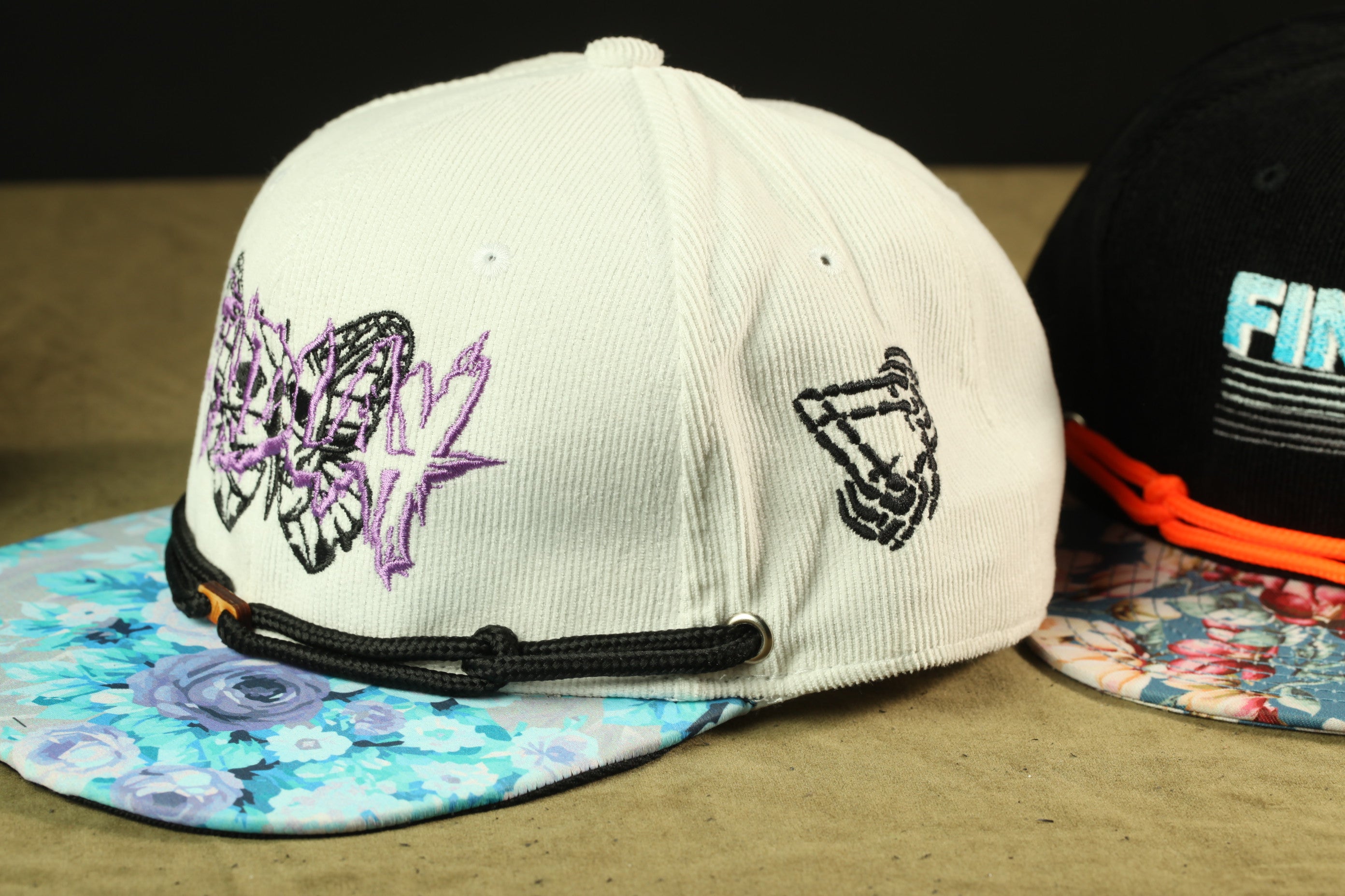 two baseball caps, one white and one black, with colorful floral patterns and embroidered designs.