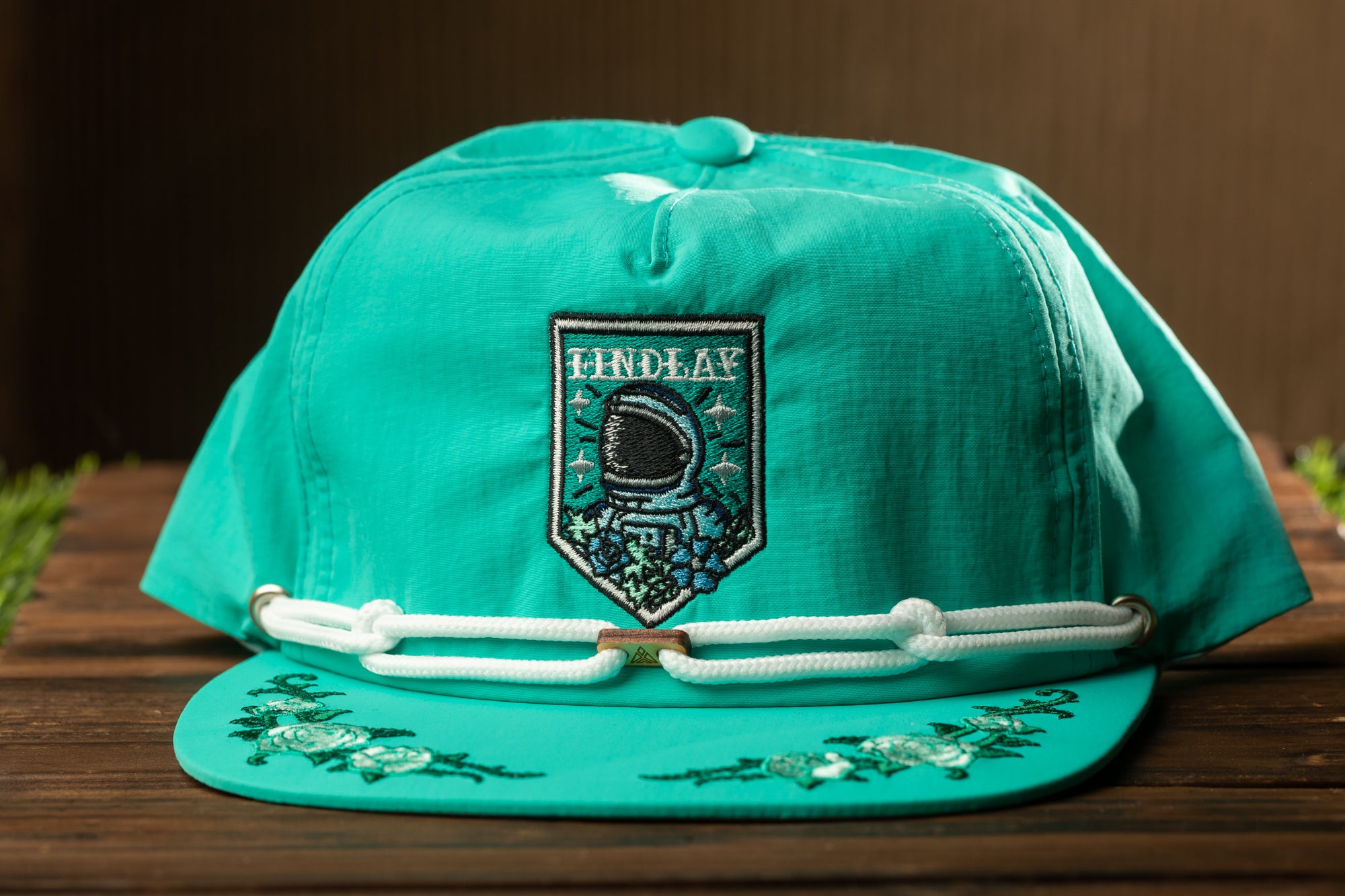 A turquoise baseball cap with a white lace trim and a patch on the front, featuring an embroidered design.