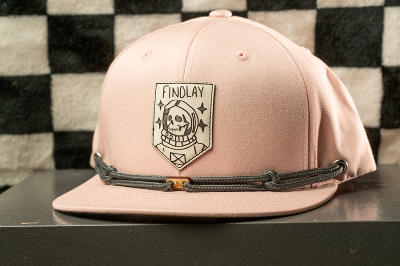 A pink baseball cap with a skull and crossbones design on the front, featuring a small patch with the text "FINDLAY" on it.