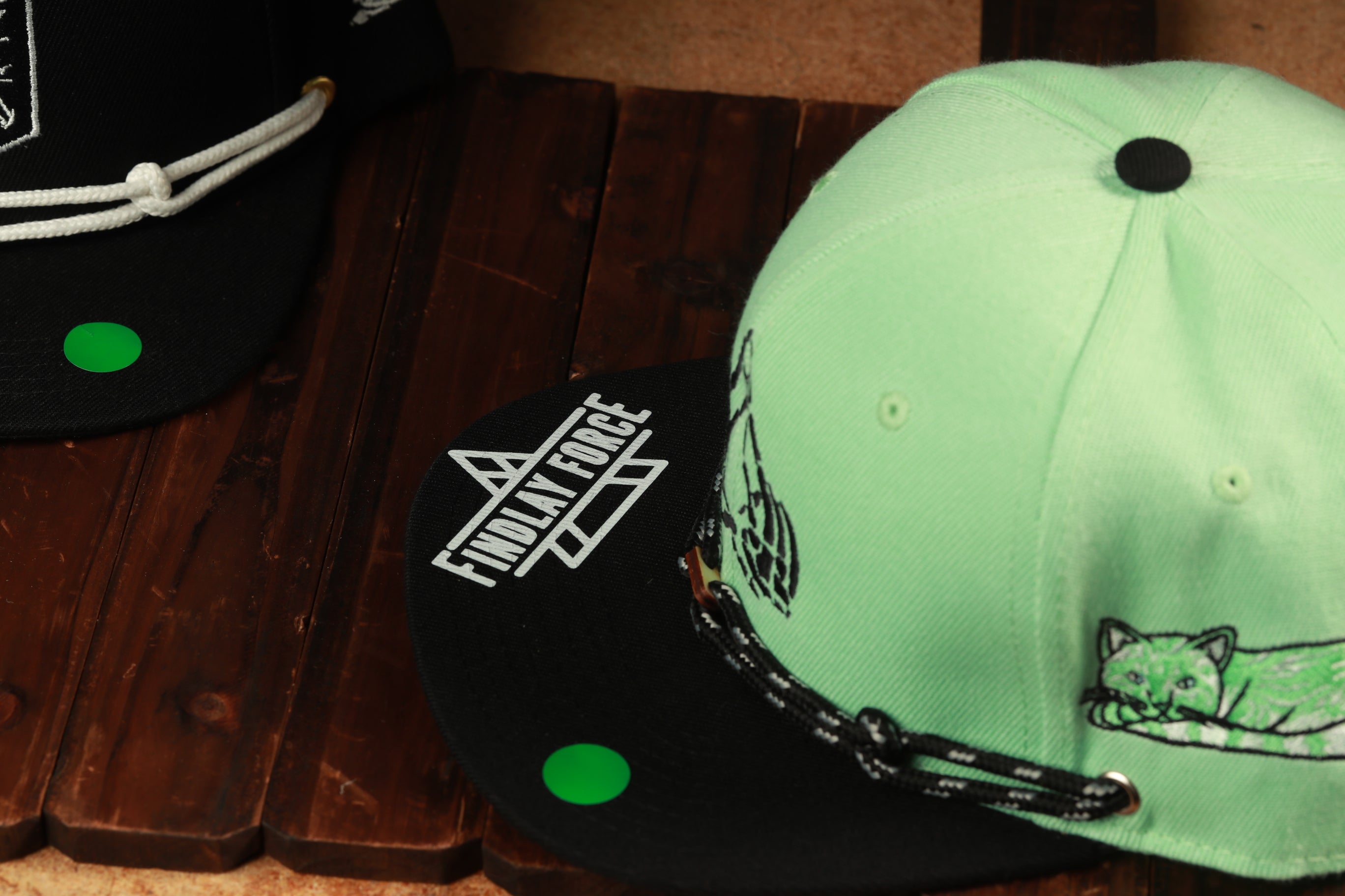 two baseball caps, one black and one green, placed on a wooden surface.