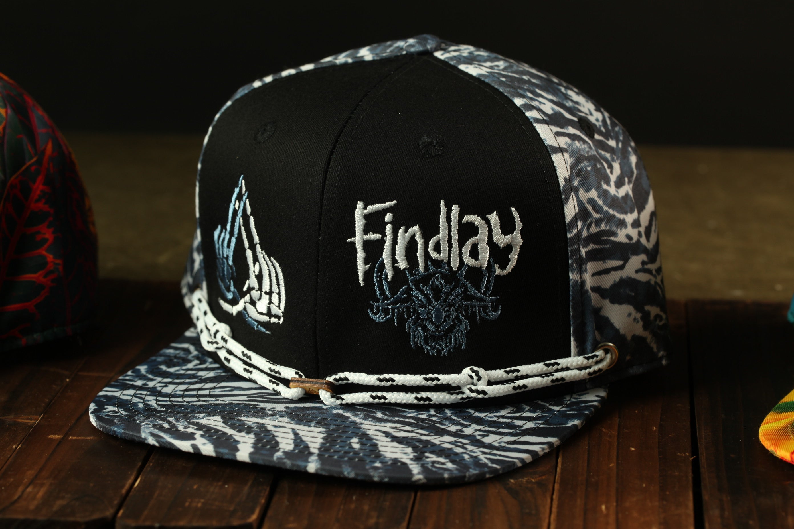 A black and white patterned baseball cap with the word "Findlay" embroidered on it, sitting on a wooden surface.