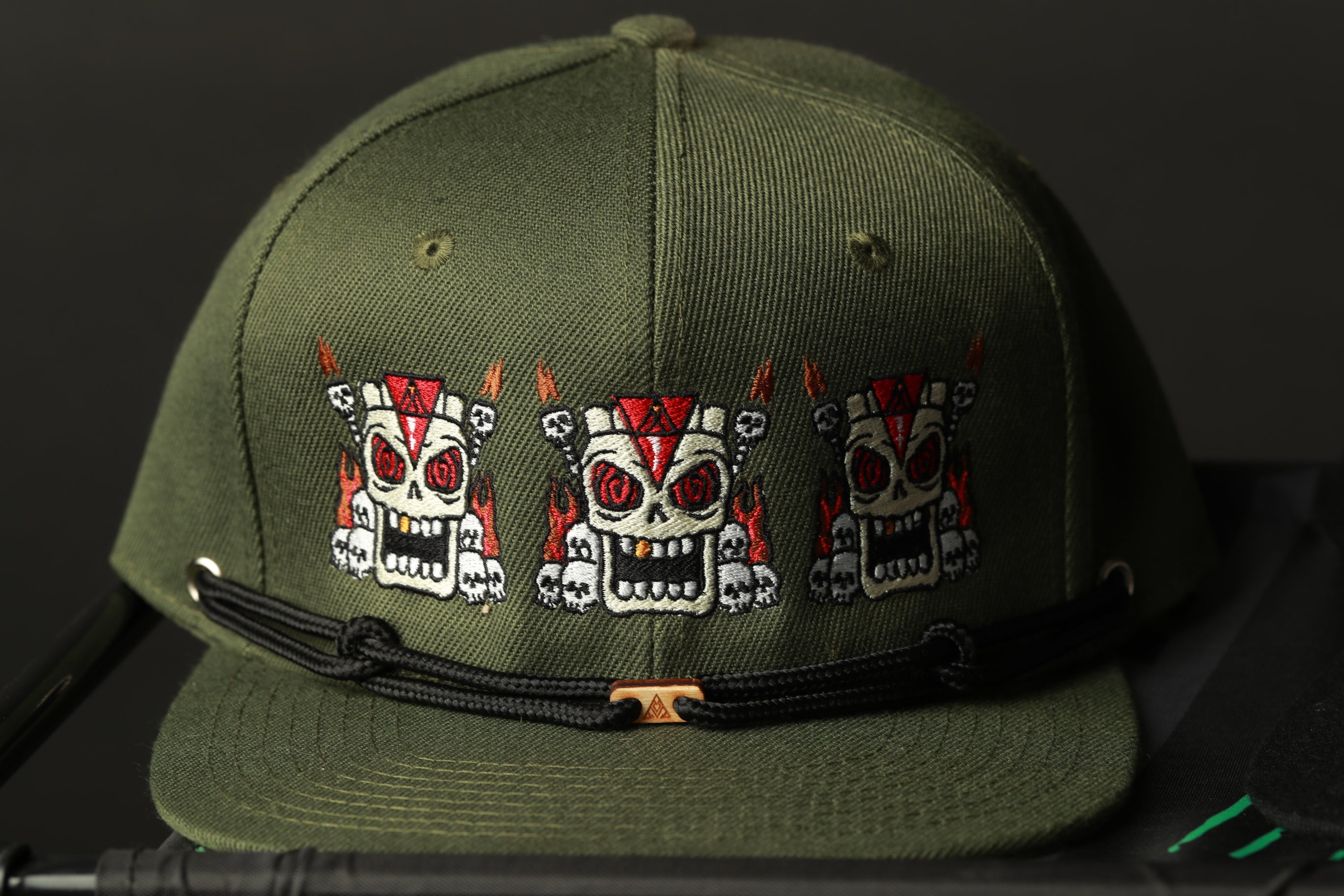 A green baseball cap with three cartoon skull designs on it.