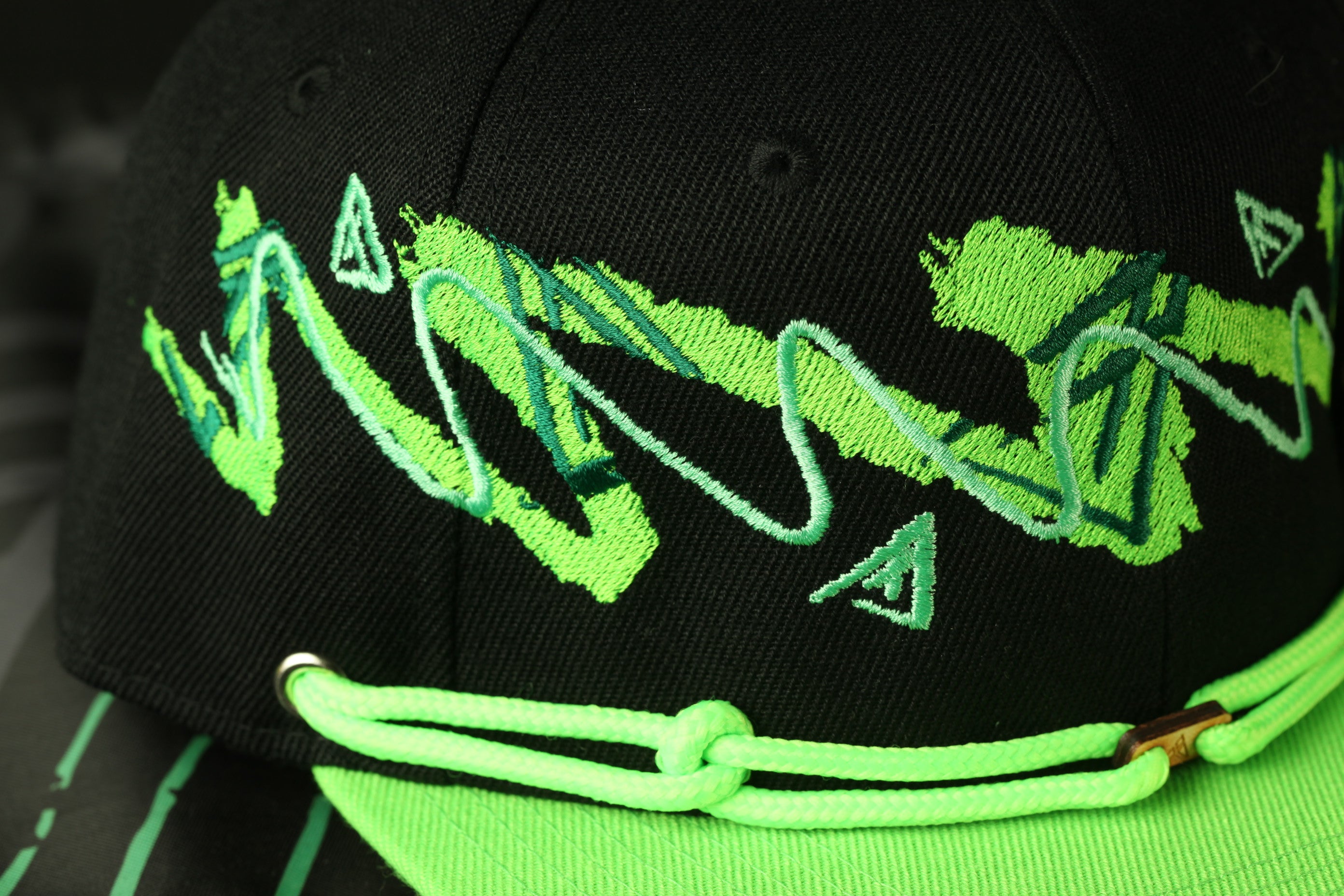 A close-up view of a black baseball cap with green and yellow embroidered designs.