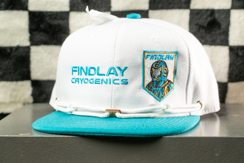 A white baseball cap with a teal brim and a logo on the front, placed on a gray surface against a checkered background.