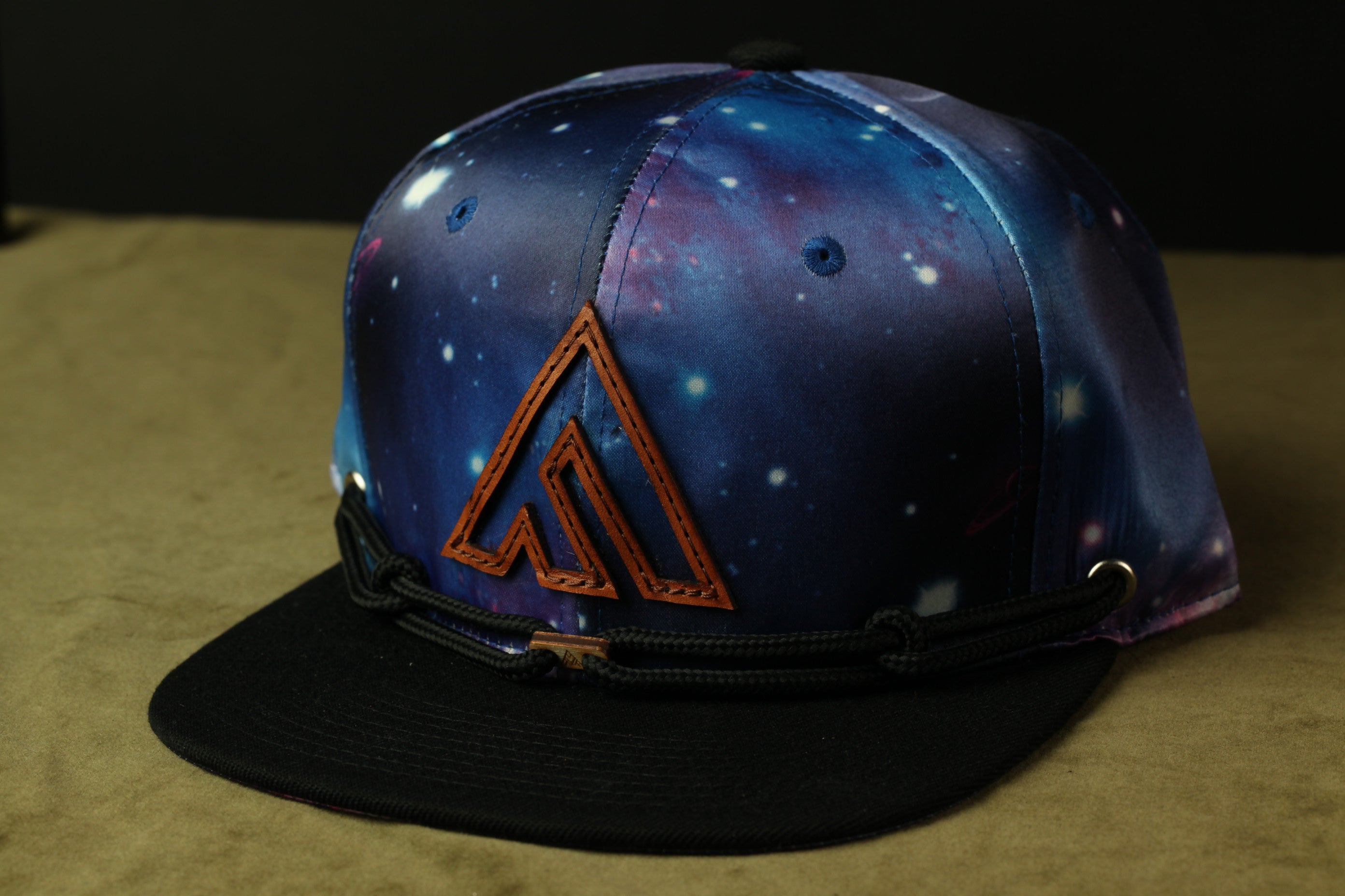 A colorful baseball cap with a space-themed design, featuring a prominent triangle logo on the front.