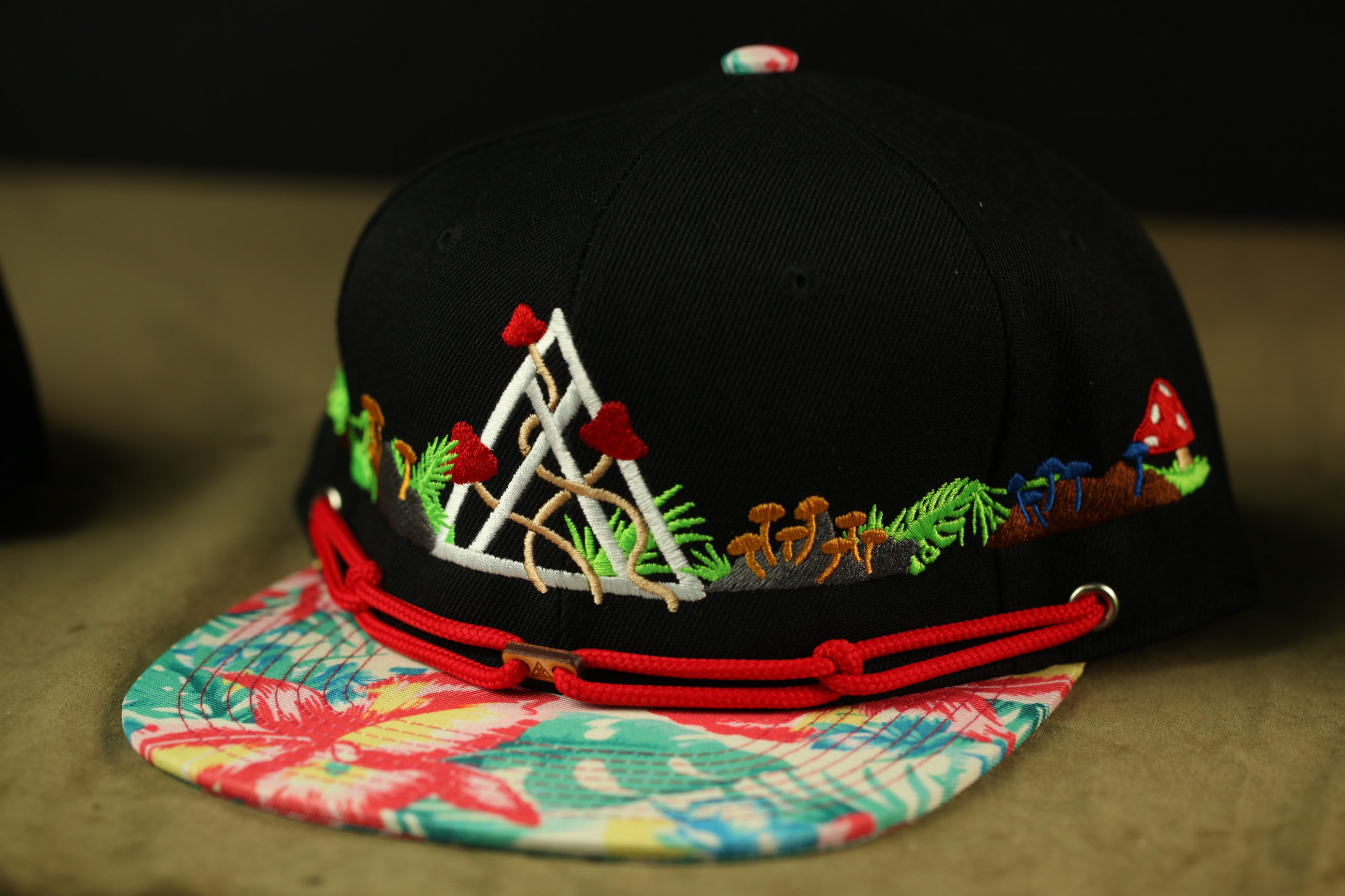 A black baseball cap with a floral pattern and a red string around the brim.