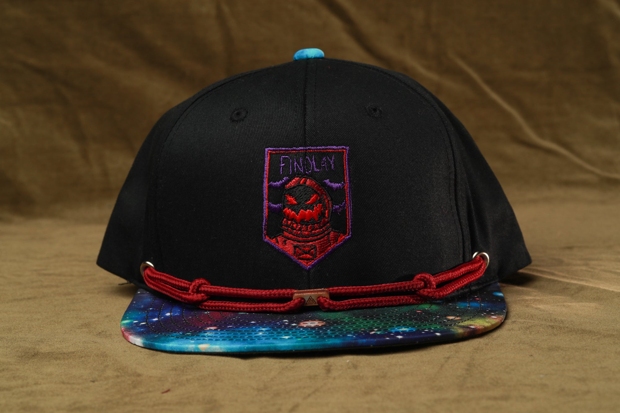 A black baseball cap with a colorful pattern on the brim and a red string around the front.