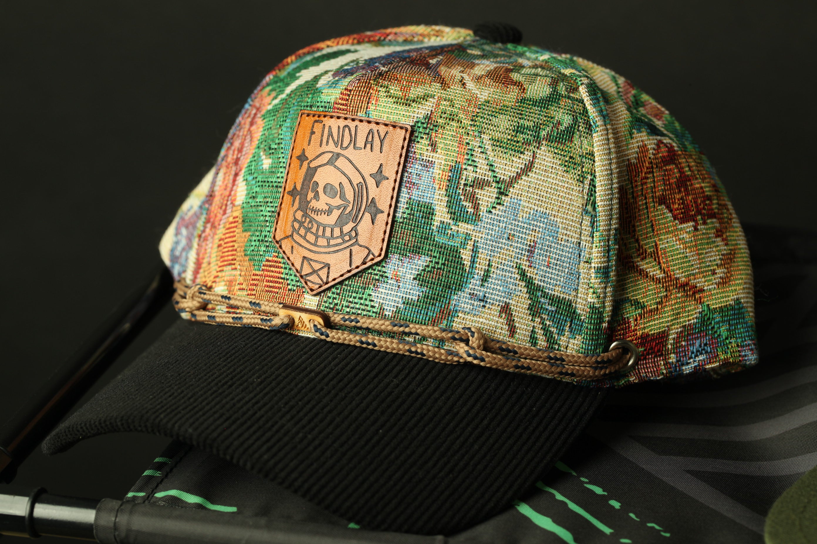 A colorful, patterned baseball cap with a leather patch on the front, resting on a black surface.