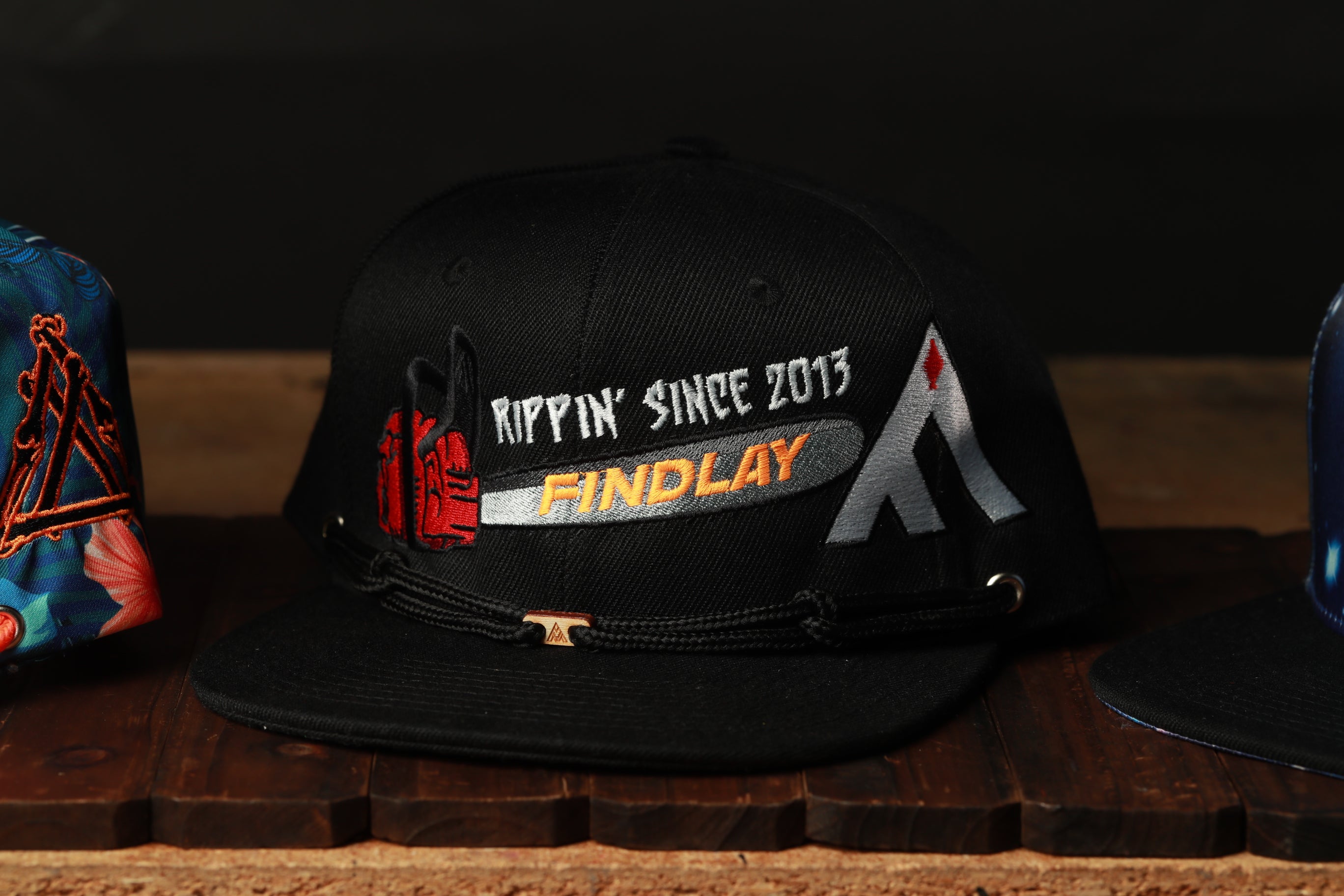 A black baseball cap with text and logos on it, placed on a wooden surface.
