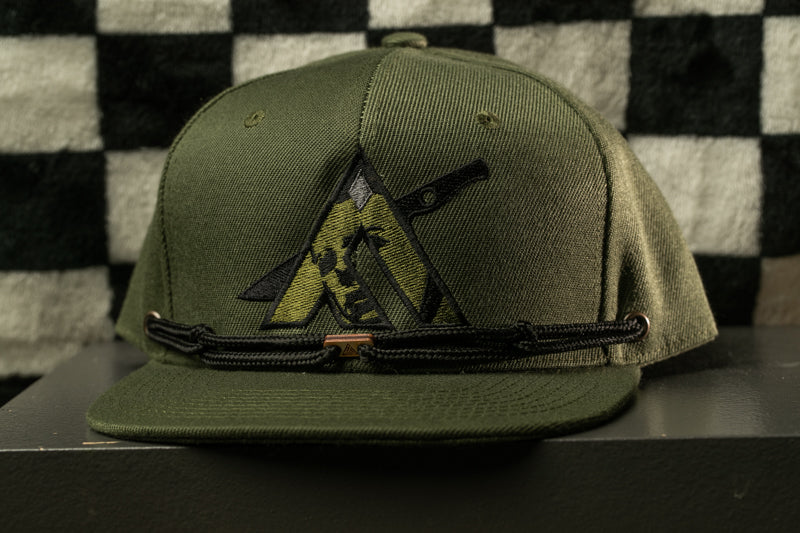 A green baseball cap with a black and yellow logo on the front, displayed on a black surface against a checkered background.