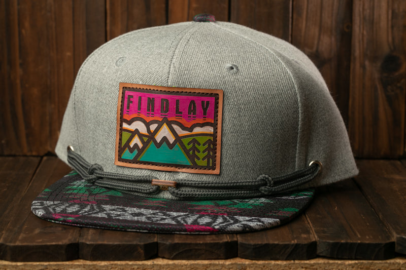 A gray baseball cap with a colorful patch on the front, featuring a mountain landscape design.