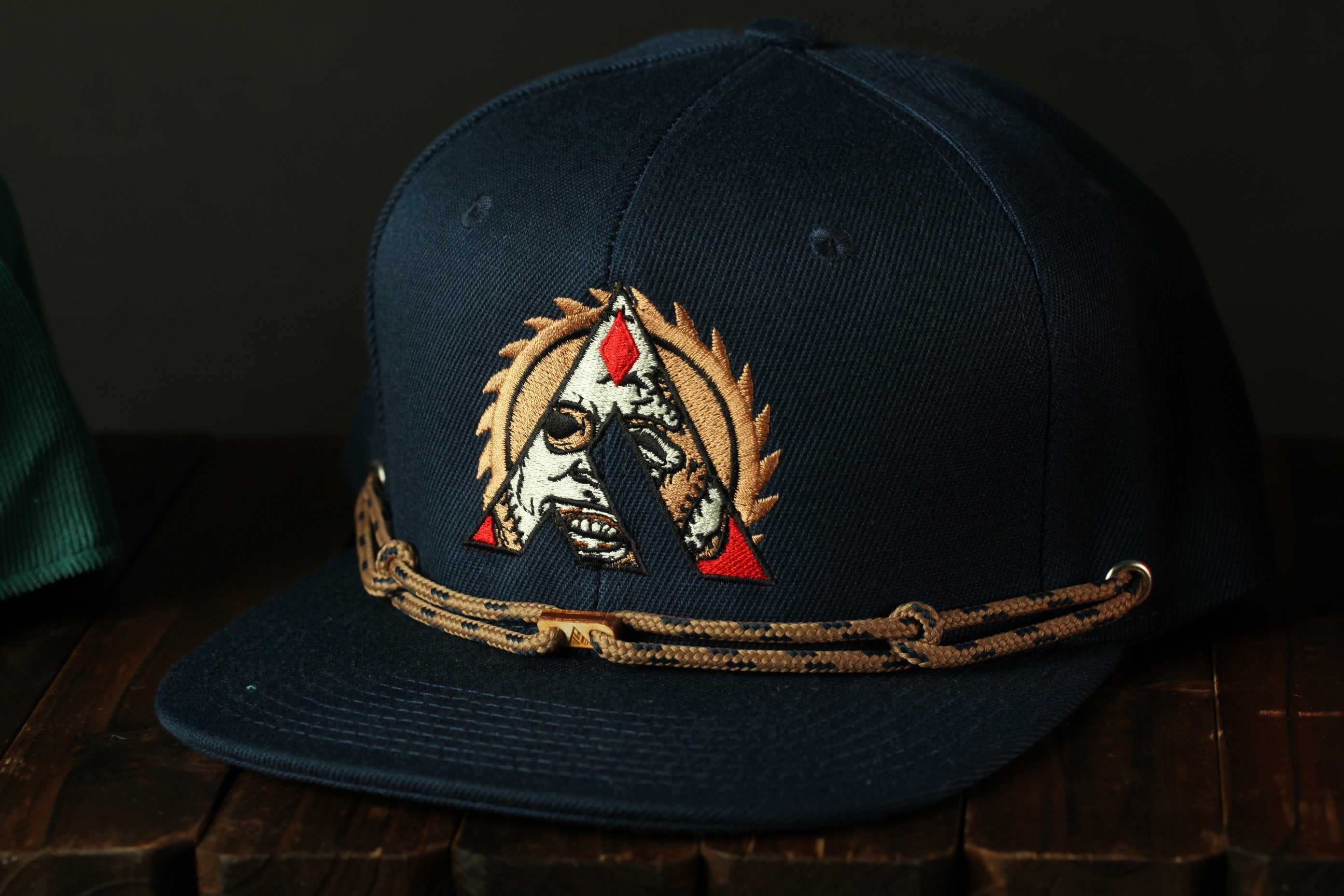 A navy blue baseball cap with a gold-colored embroidered logo on the front, sitting on a wooden surface.