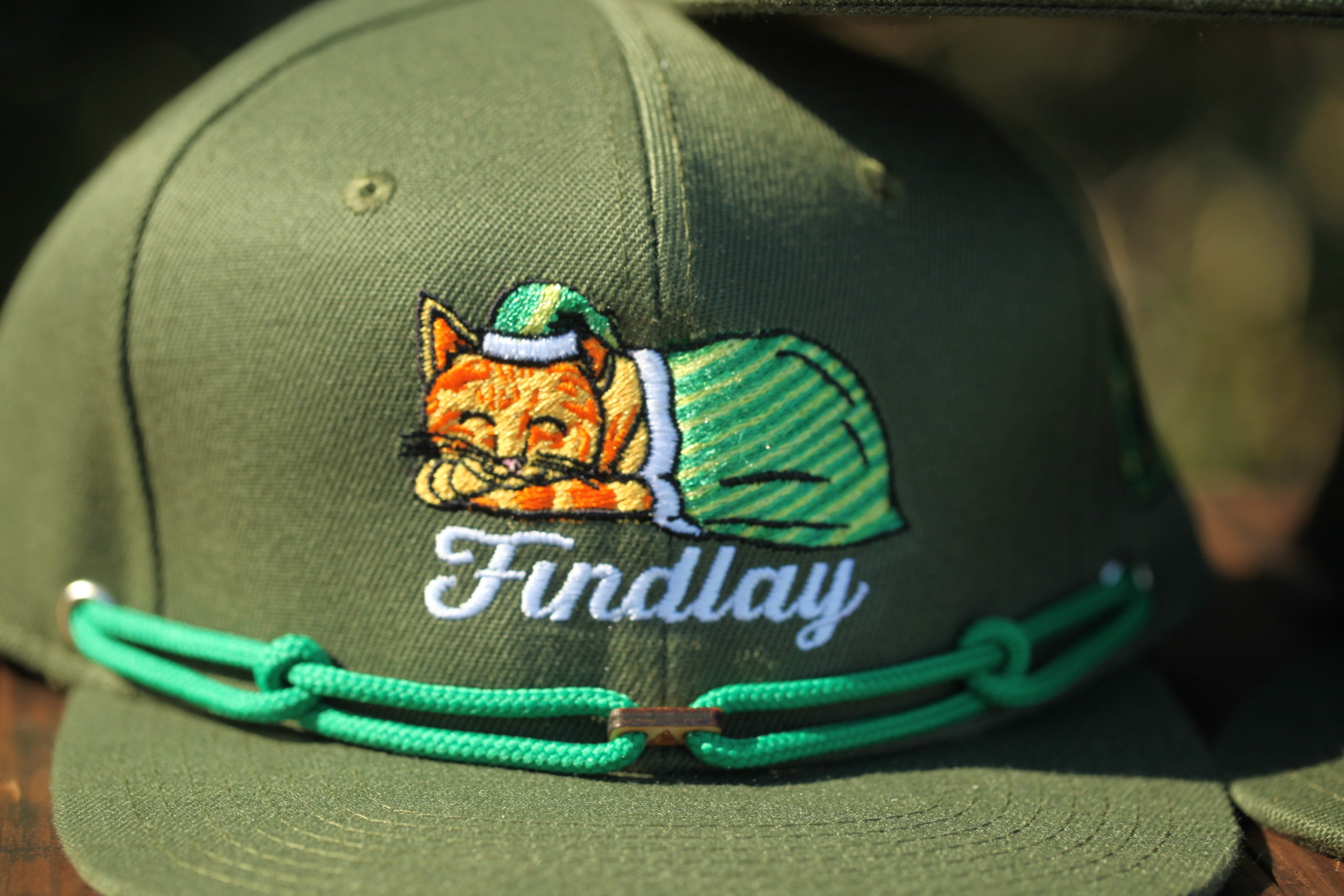 A green baseball cap with a cat embroidered on it, wearing a green hat and a green scarf.