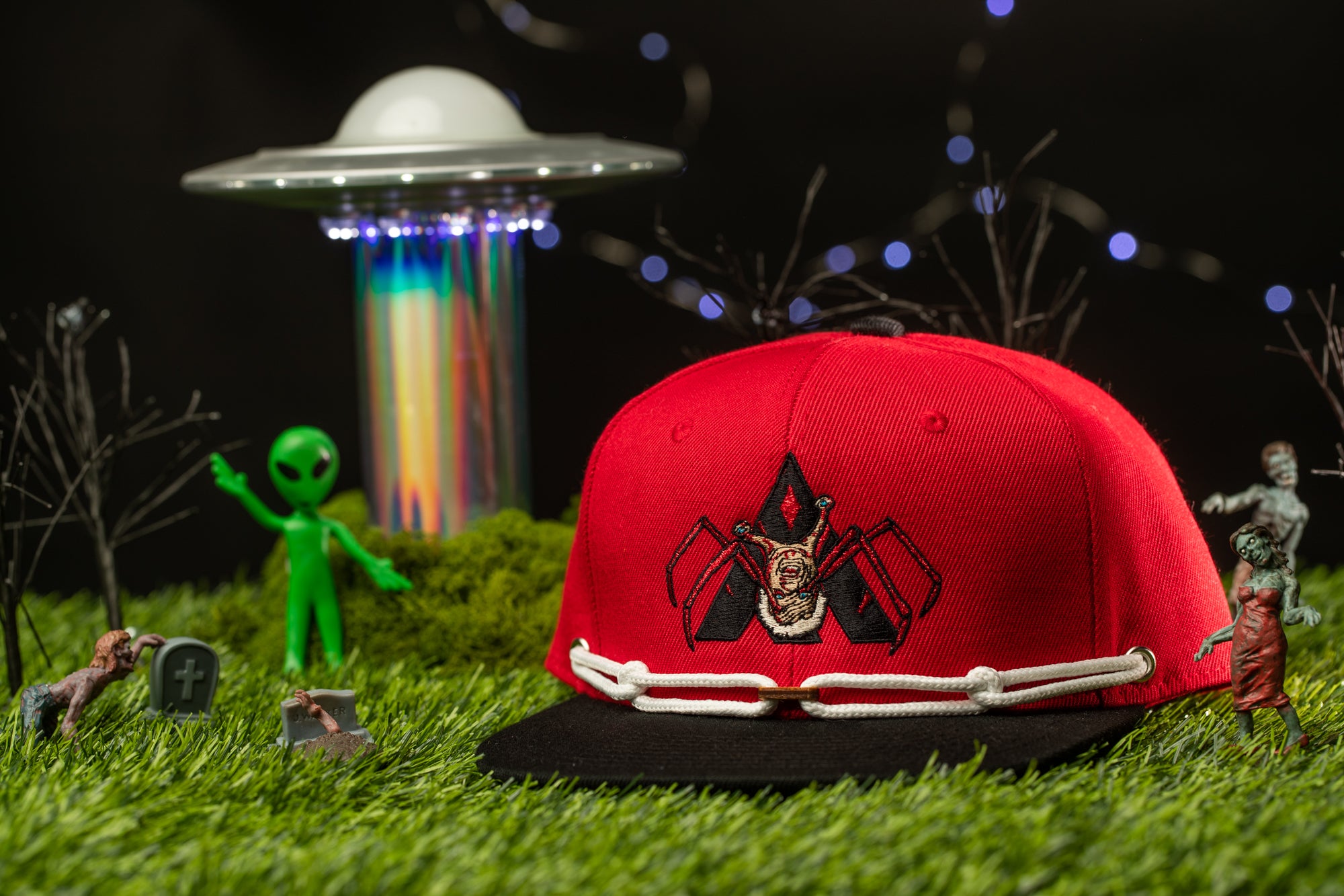 a red baseball cap with a black and white design, surrounded by various toy figures and a spaceship in a grassy area.