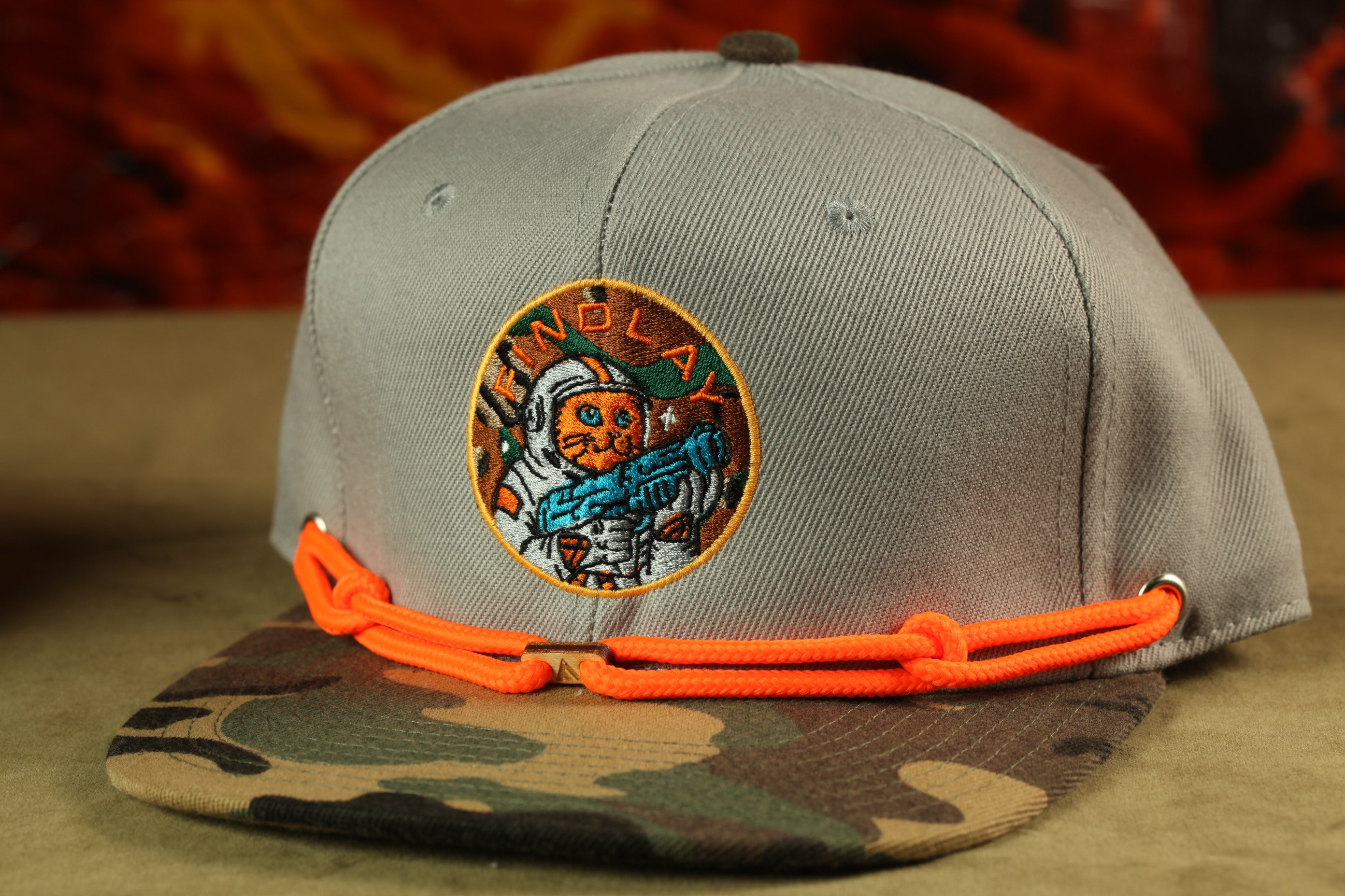 A gray baseball cap with a camouflage pattern and an embroidered patch featuring a cat wearing a spacesuit.