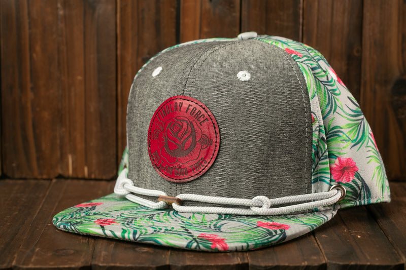 A gray baseball cap with a red circular logo and a floral pattern on the brim, placed on a wooden surface.
