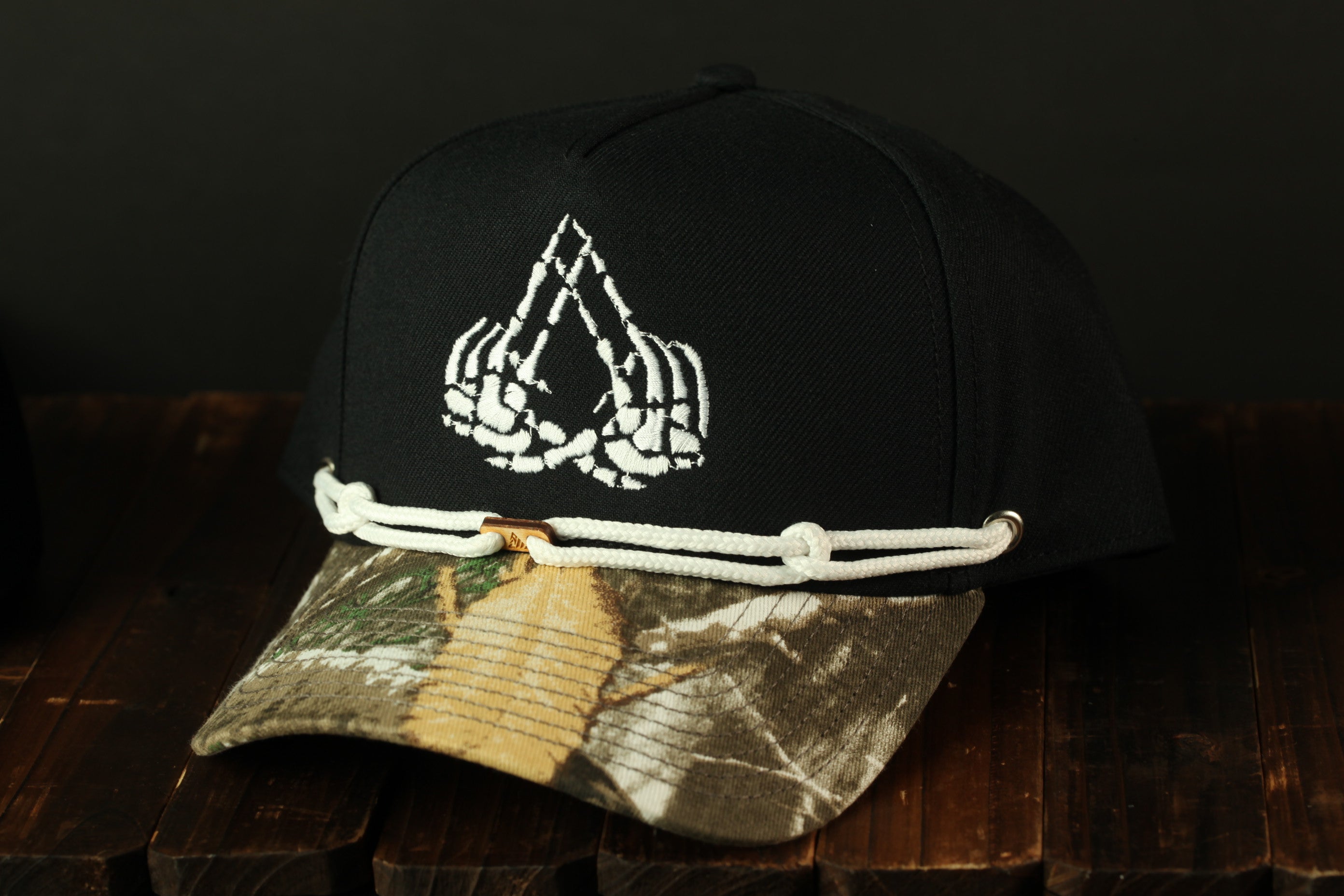 A black baseball cap with a camouflage pattern and a white skull and crossbones design on the front.