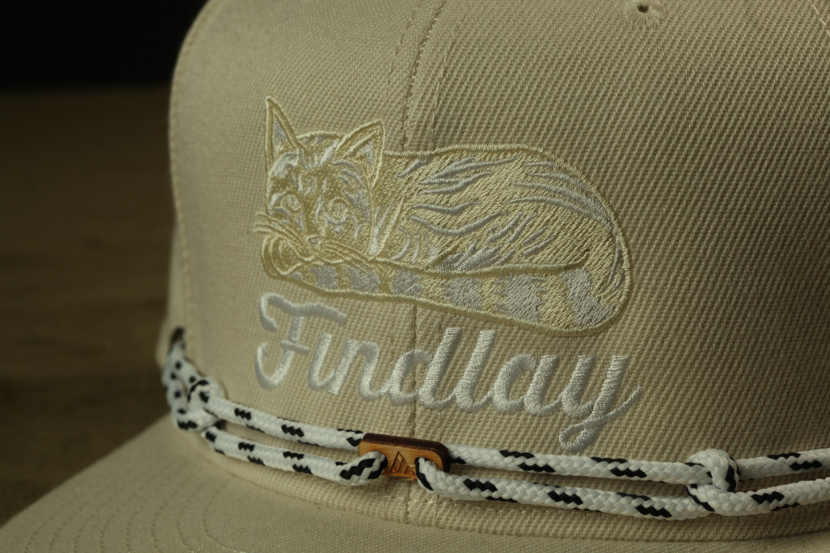 A close-up of a beige baseball cap with a cat embroidered on it, and the word "Findlay" written on the front.