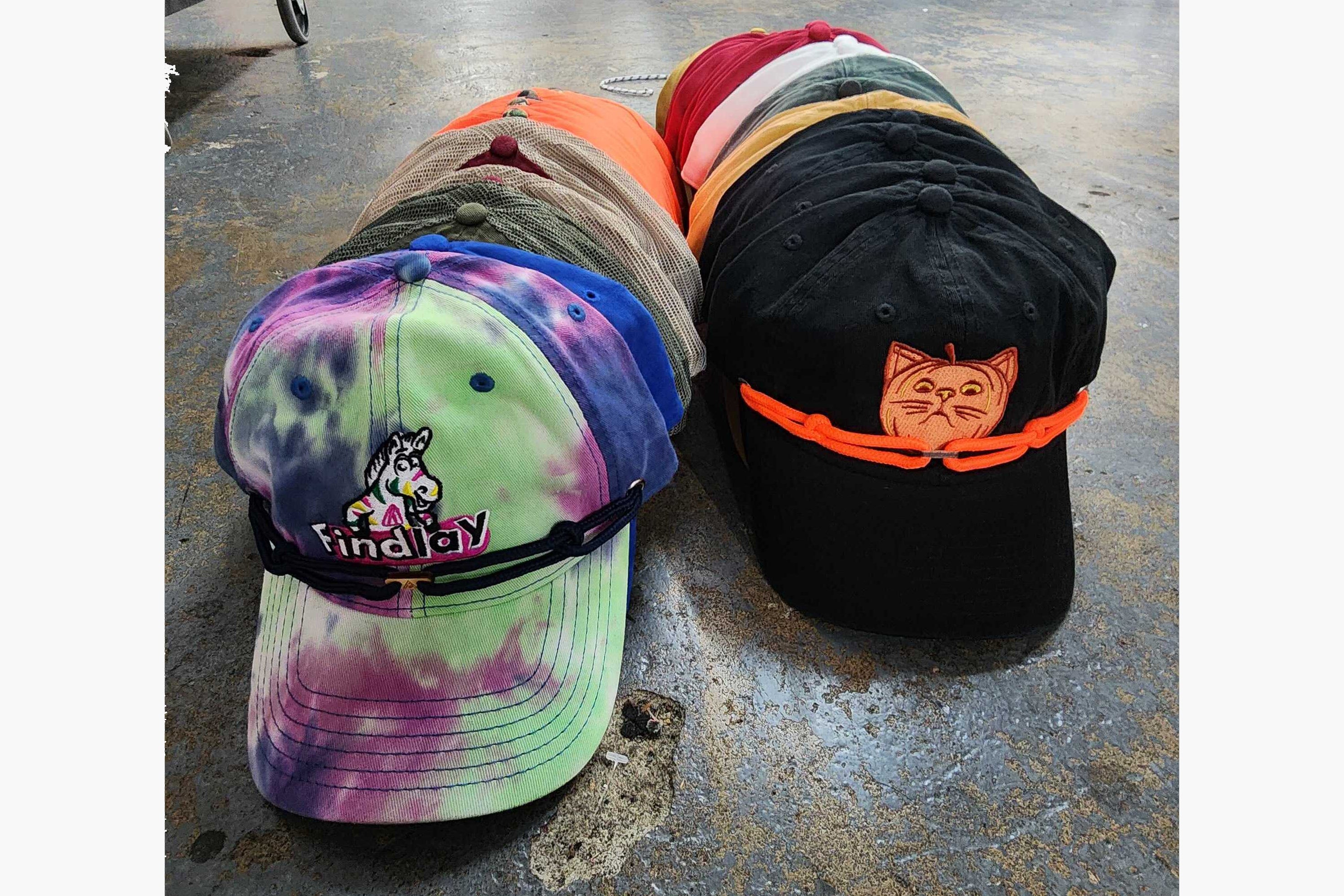 A collection of colorful baseball caps is neatly arranged on a concrete floor.