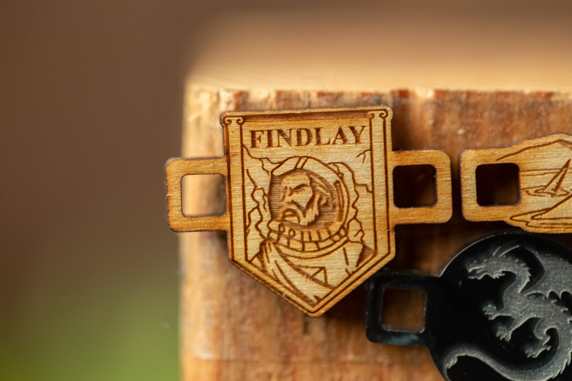 a wooden badge with a dragon design, and a black metal object with a dragon design, both placed on a wooden surface.